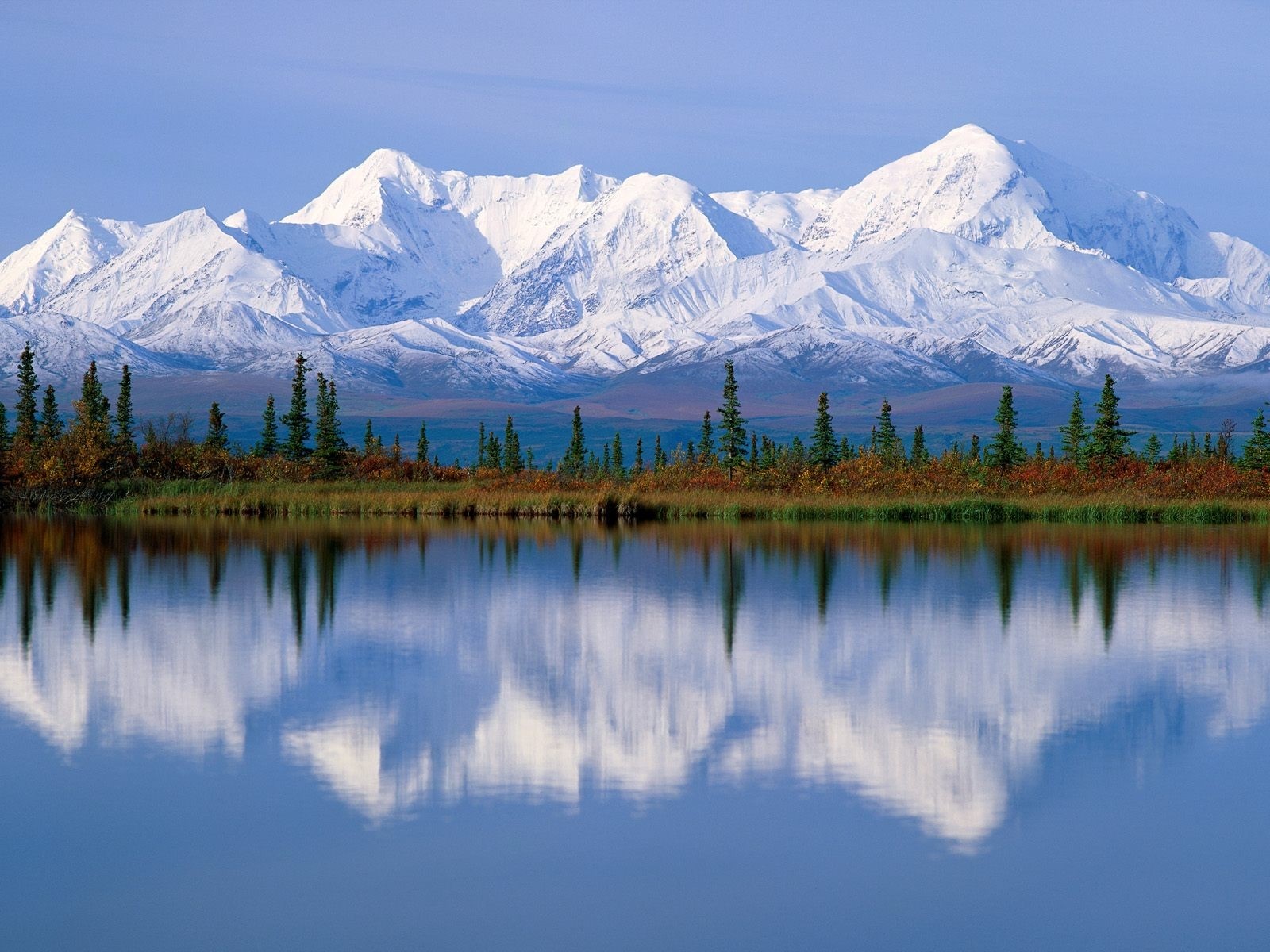 Snow-capped mountains reflected in a calm lake with evergreen trees HD Wallpaper