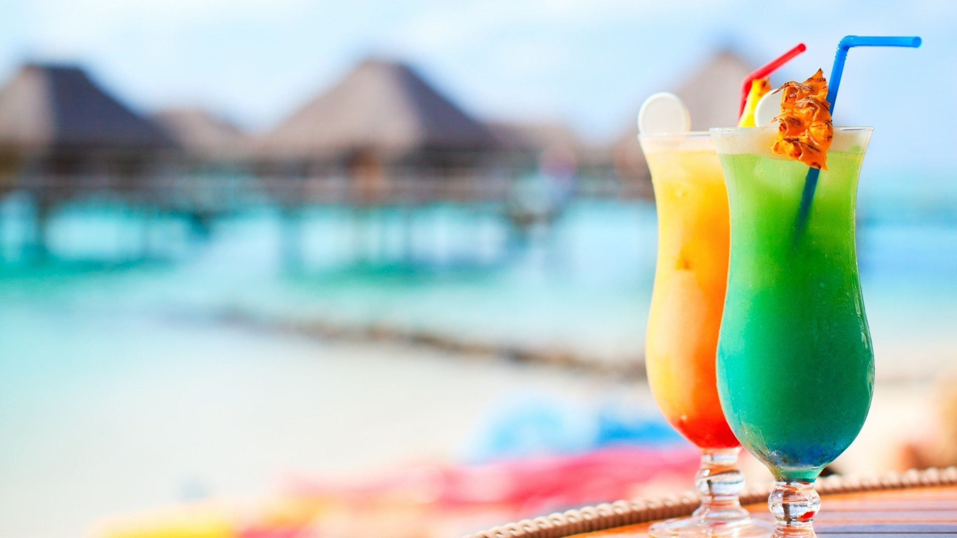 Two colorful cocktails on a table with a beach resort in the background HD Wallpaper