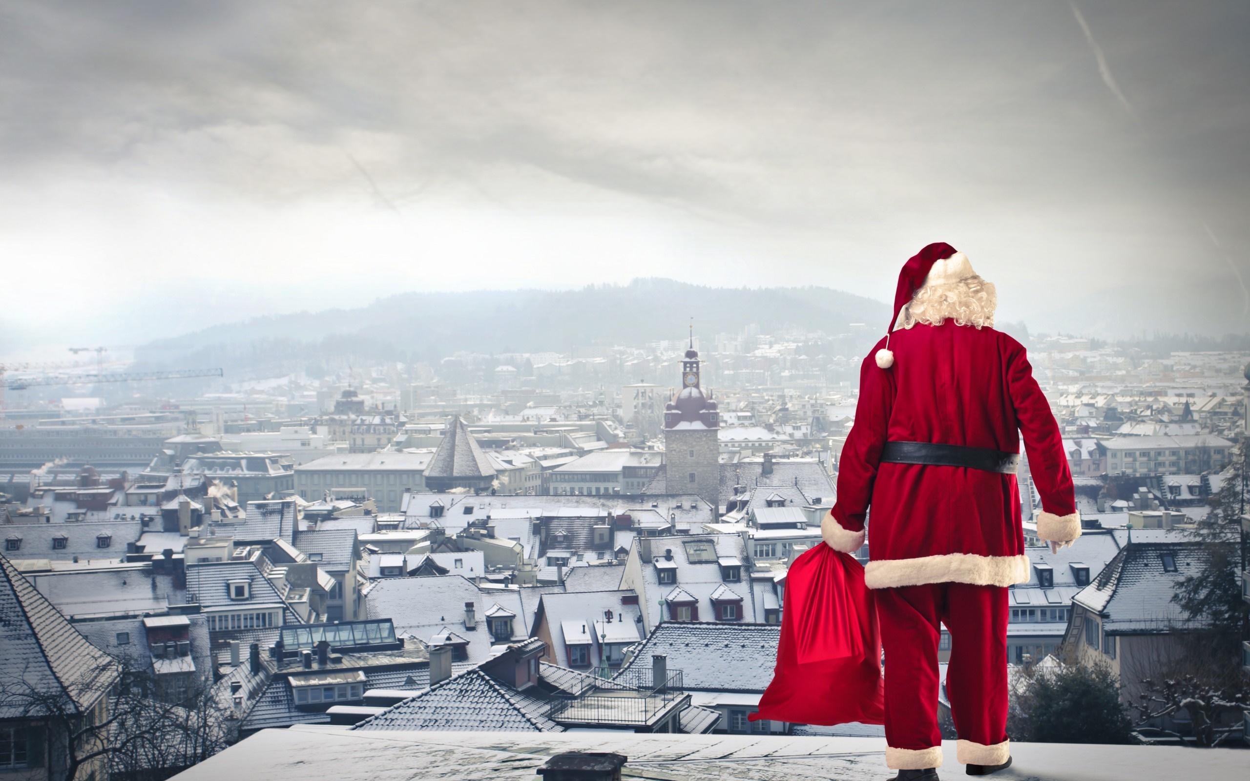 Santa Claus with a gift bag overlooking a snowy city HD Wallpaper