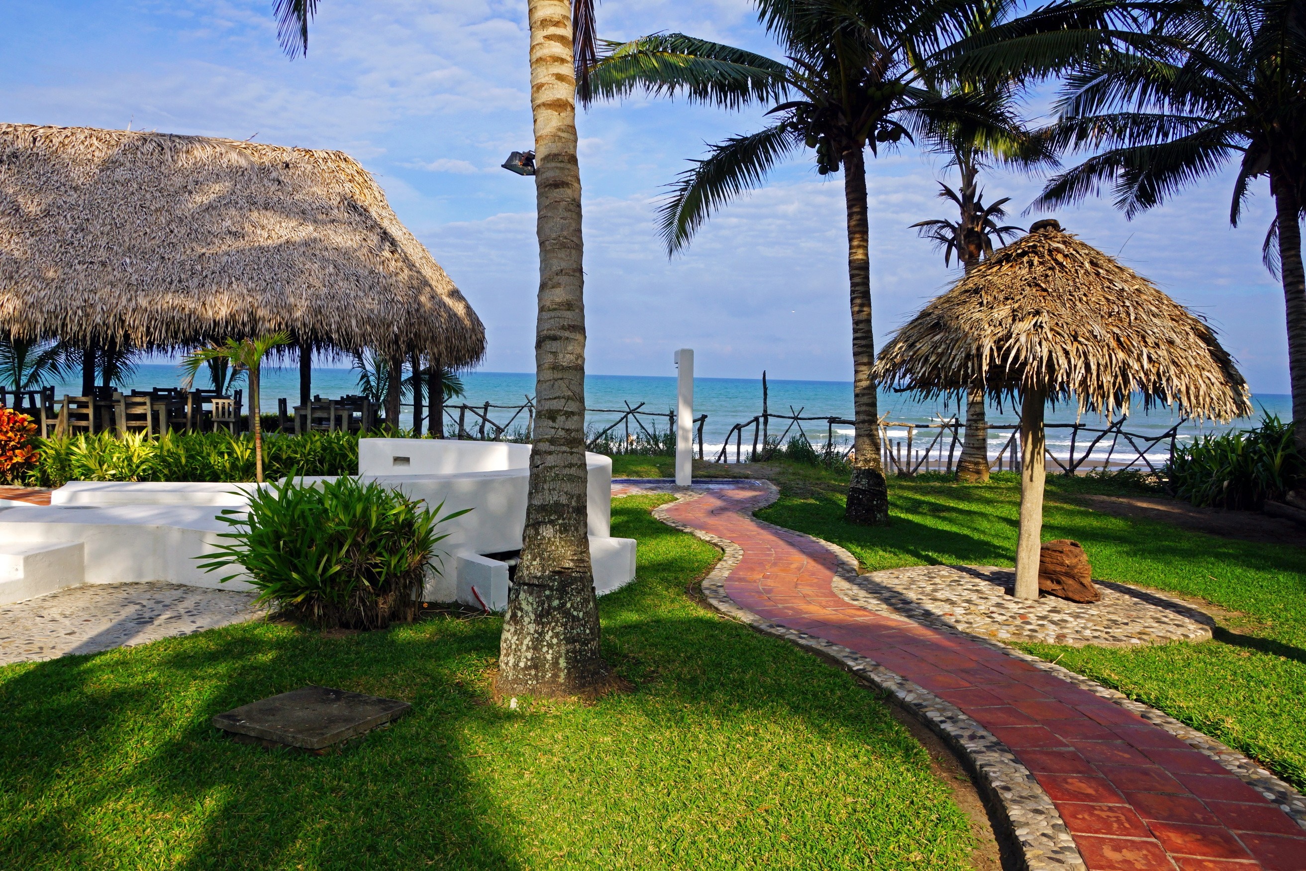 Tropical resort with thatched roofs and palm trees by the ocean HD Wallpaper