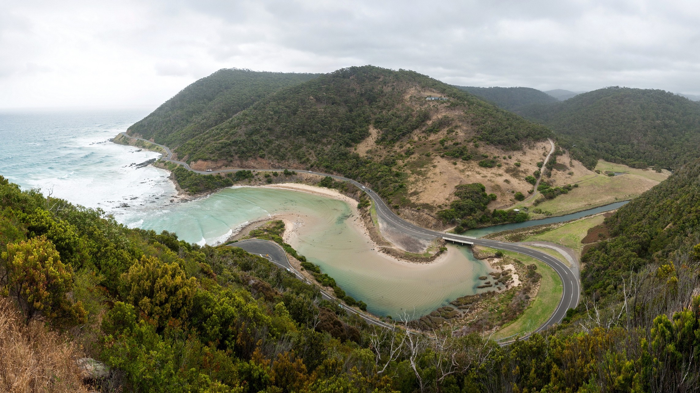 Coastal highway winding around a bay with forested hills HD Wallpaper