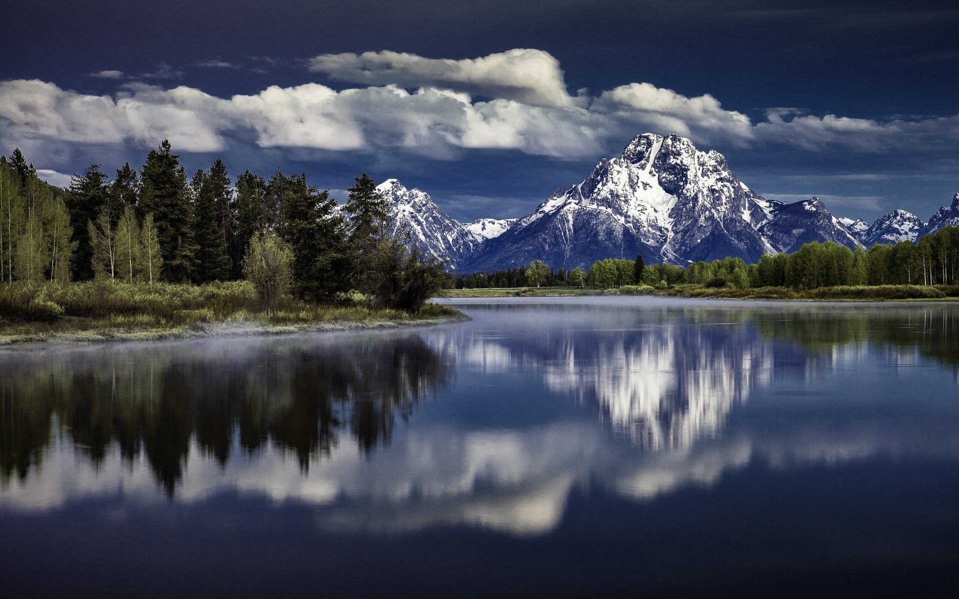 Snow-capped mountains reflected in a calm lake with trees HD Wallpaper