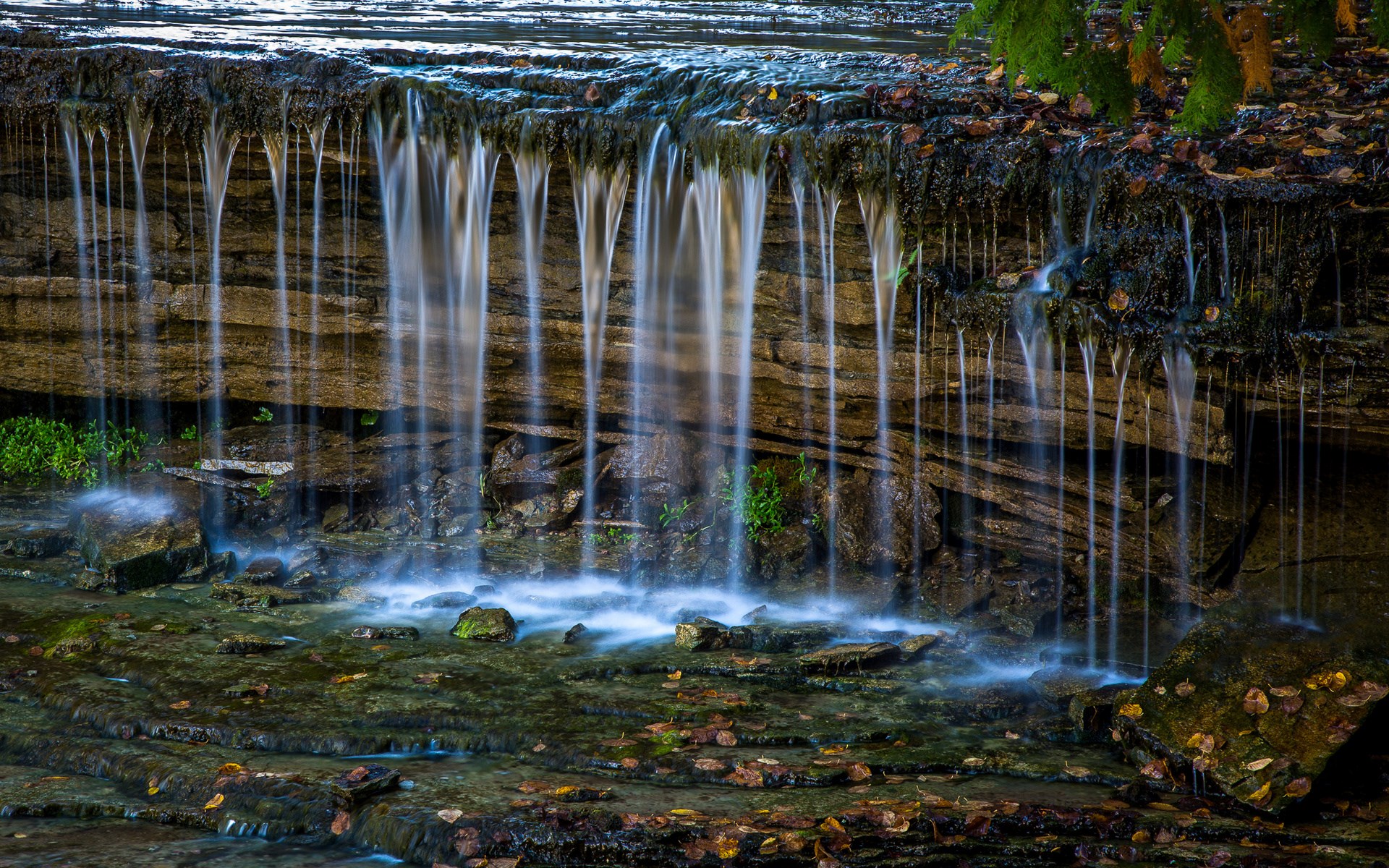 Waterfall cascading over layered rocks HD Wallpaper