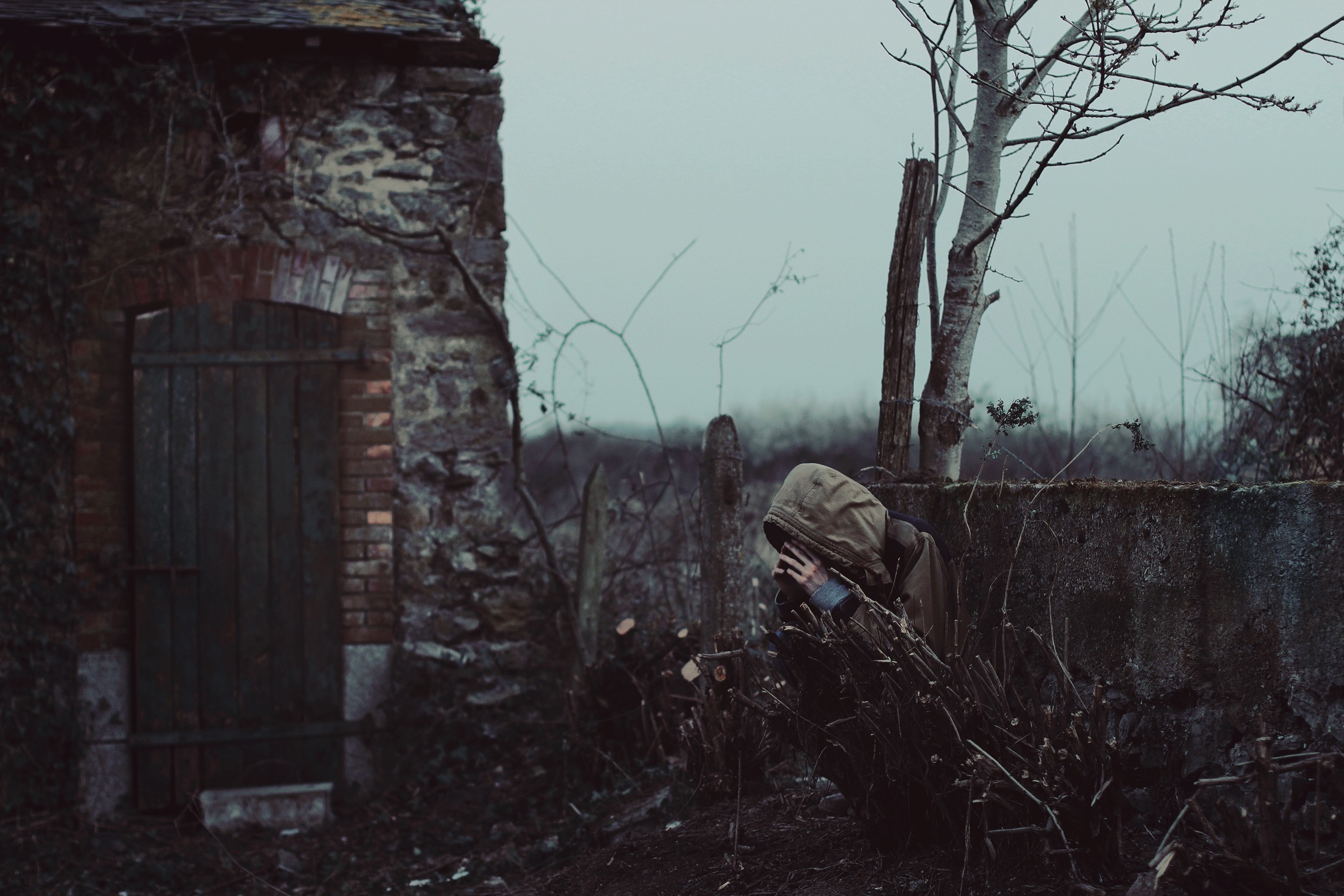 Person in hood hiding behind wall near old building HD Wallpaper