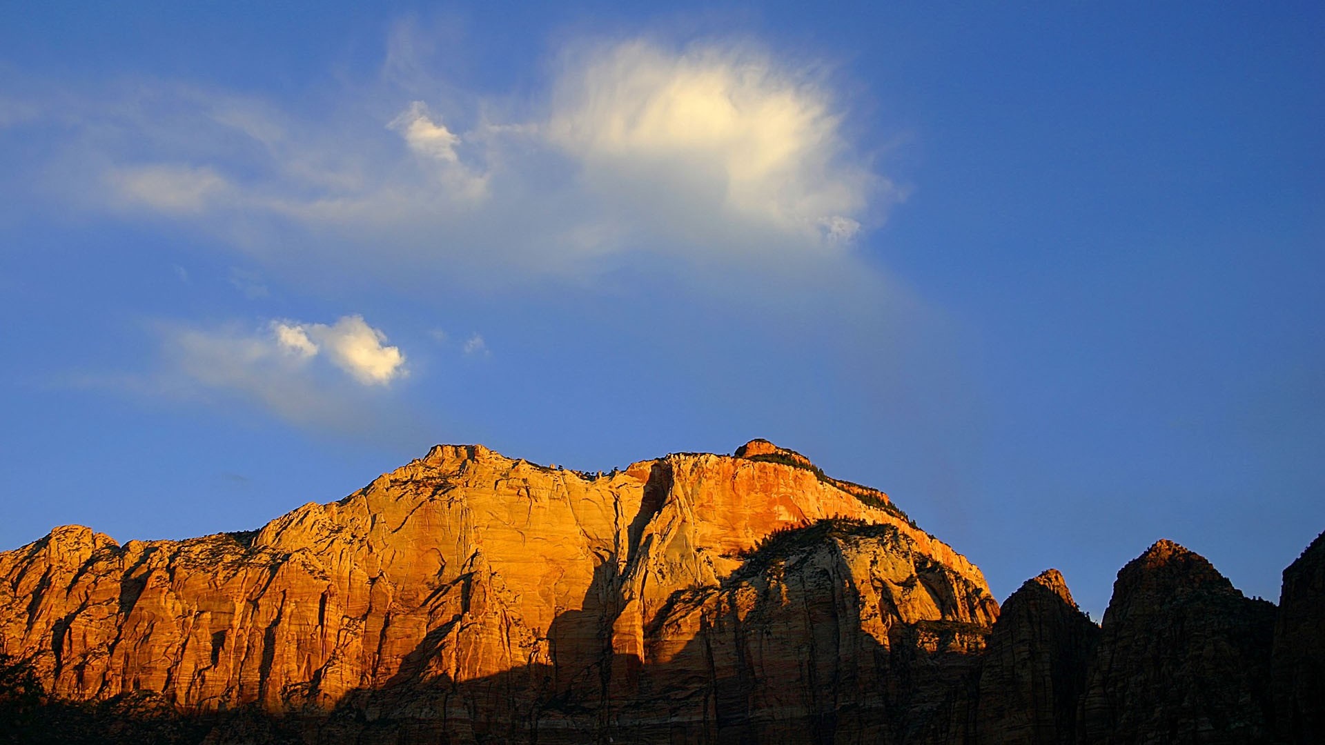 Mountain range illuminated by sunset under a blue sky with clouds HD Wallpaper