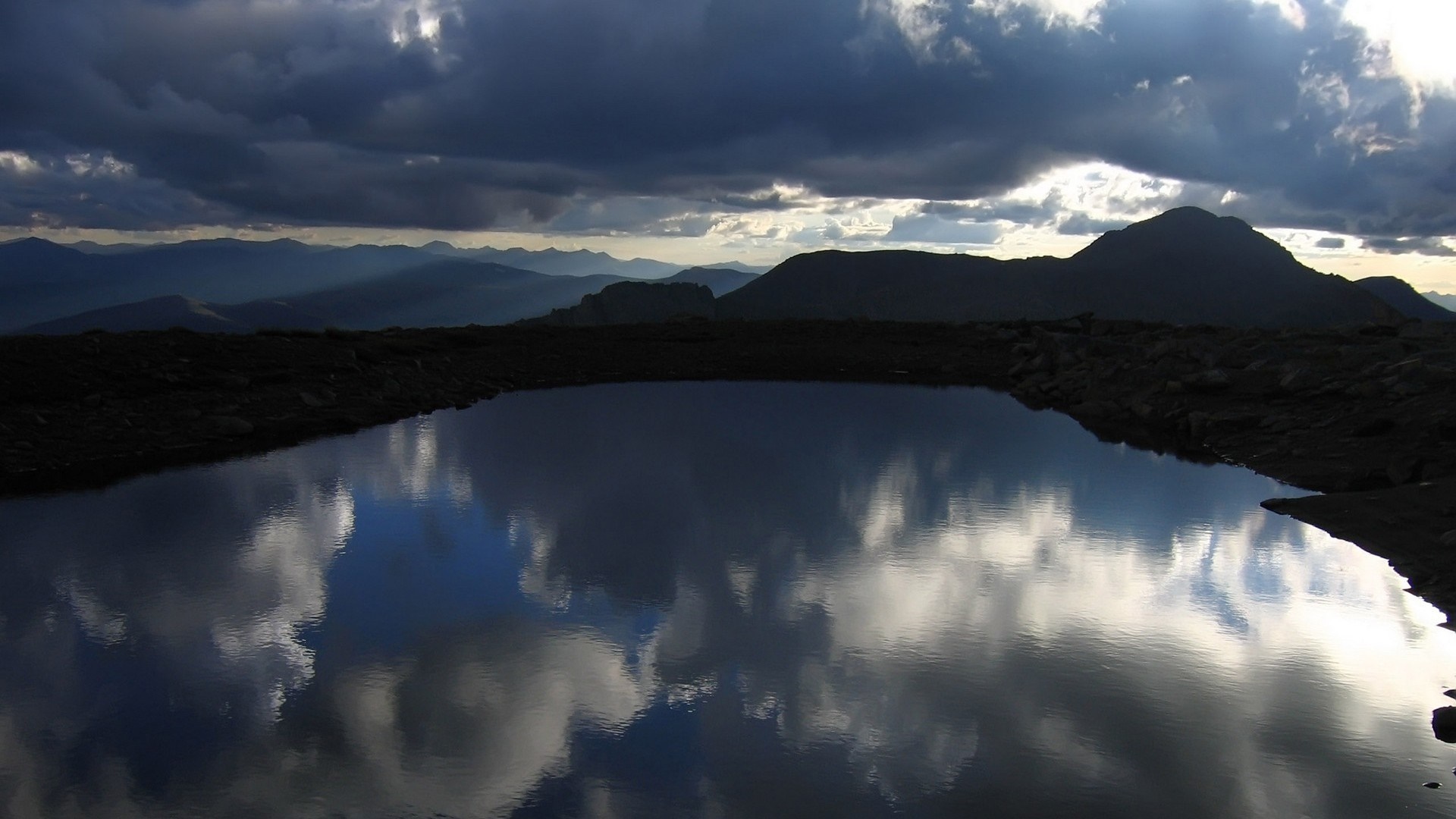 Mountain lake reflecting dramatic clouds and peaks HD Wallpaper