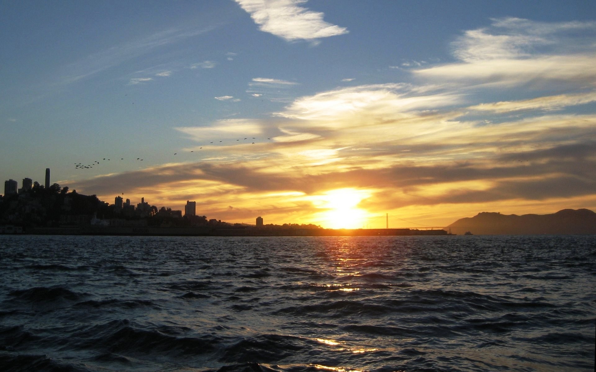 Sunset over the ocean with city skyline and mountains HD Wallpaper