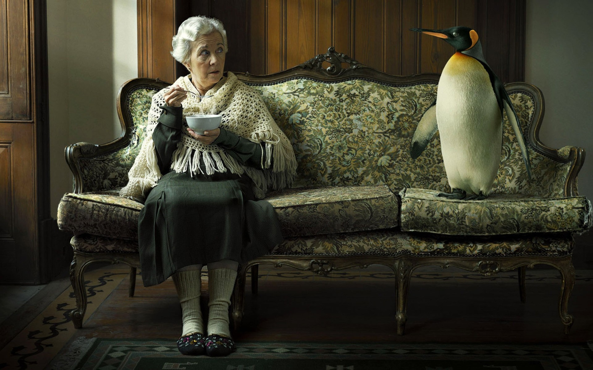 Elderly woman eating soup with a penguin on a couch HD Wallpaper