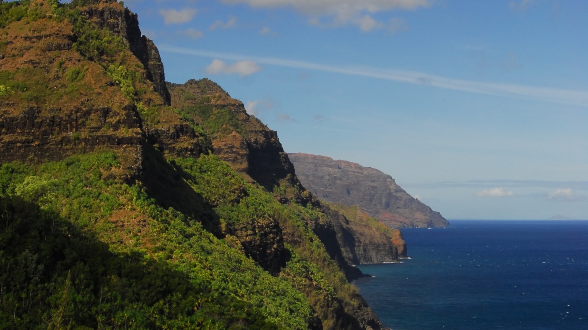 Rugged green mountains meet the blue ocean under a cloudy sky HD Wallpaper