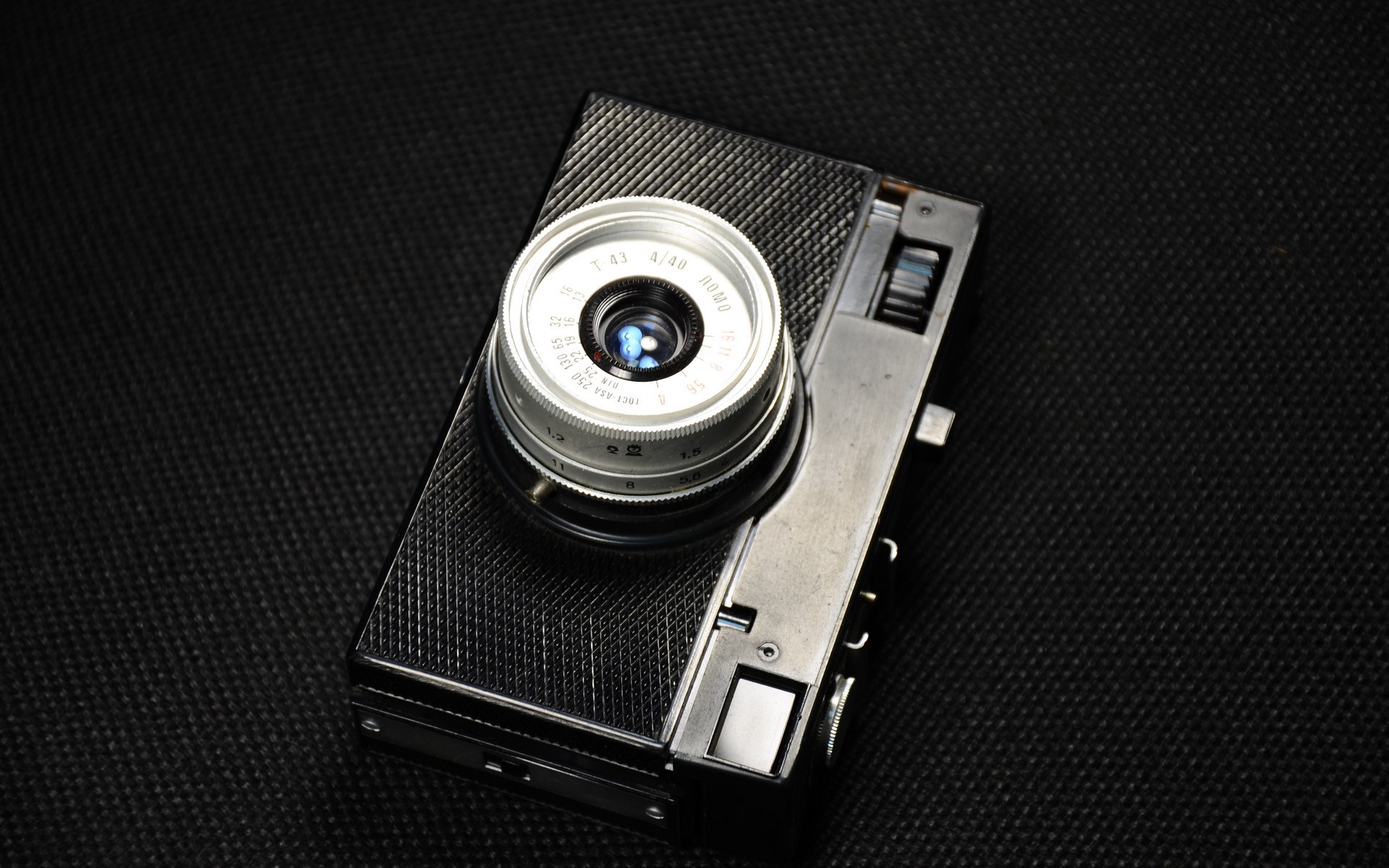 Vintage camera with a silver lens on a black textured surface HD Wallpaper