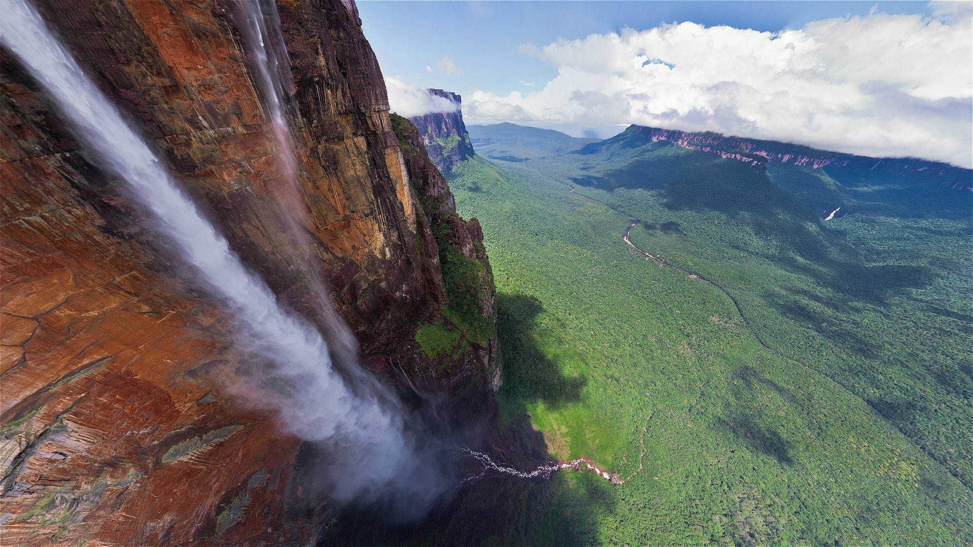 Waterfall cascading down a massive cliff into a lush green valley HD Wallpaper