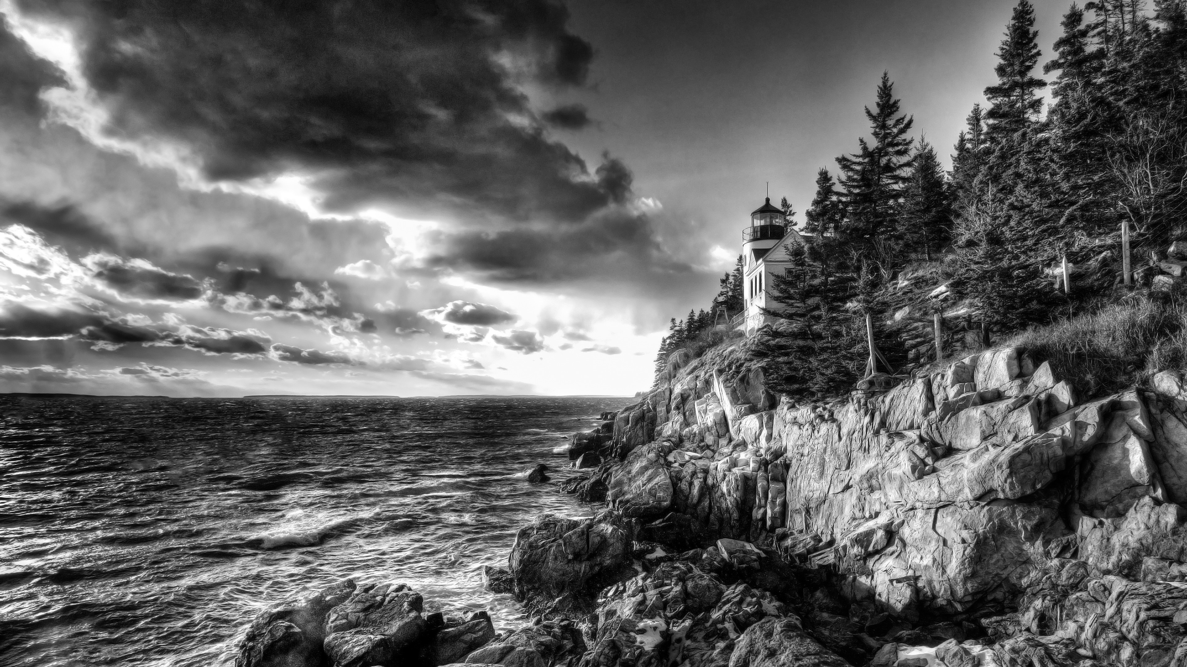 Monochrome lighthouse on a rocky coast with stormy sea HD Wallpaper