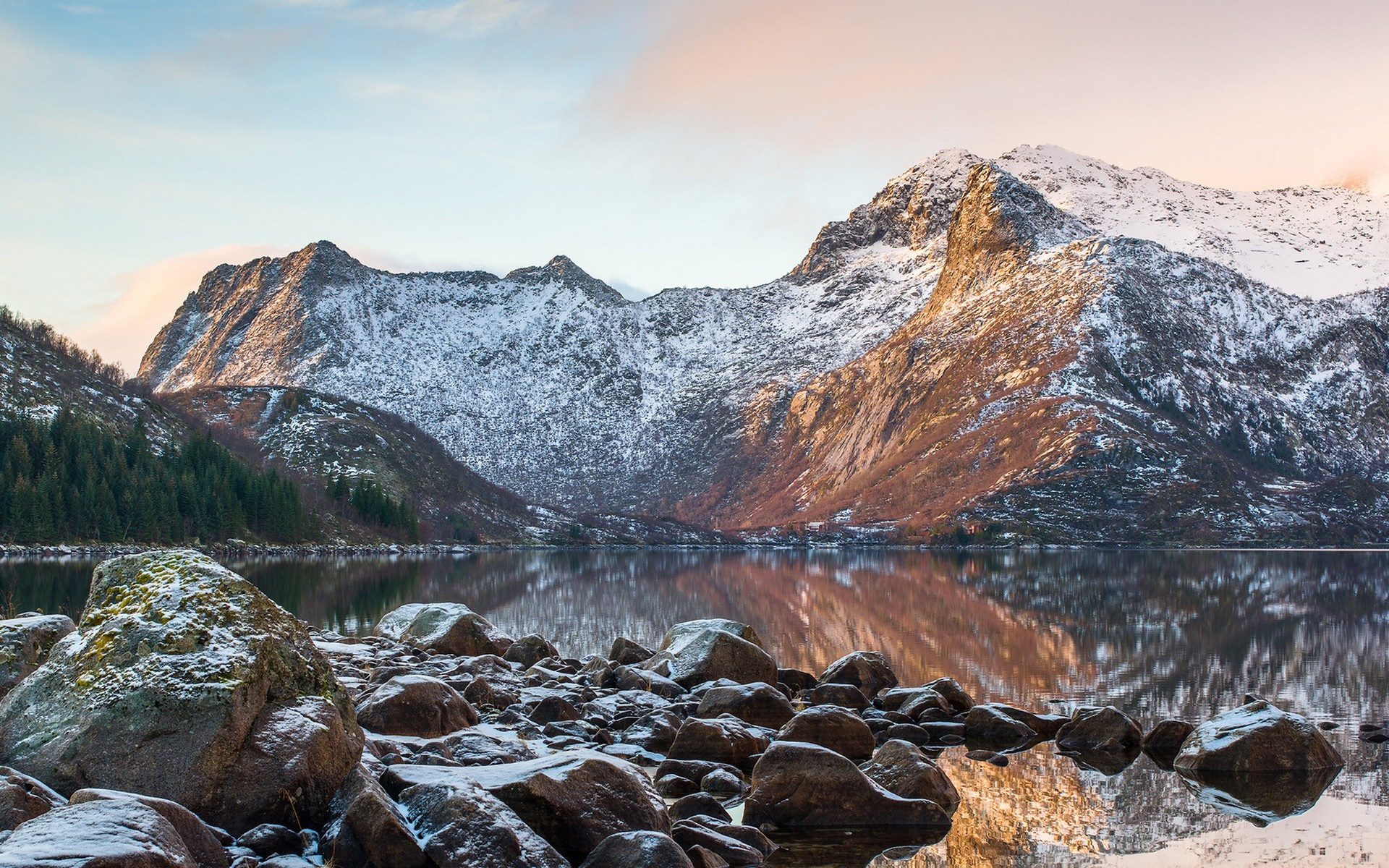 Snow-capped mountains reflected in a calm lake with rocks in the foreground HD Wallpaper