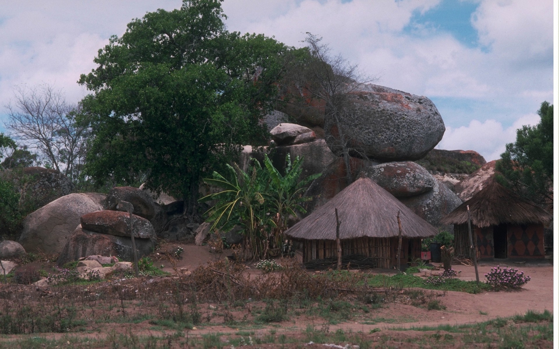 Traditional huts nestled among large granite boulders and trees HD Wallpaper