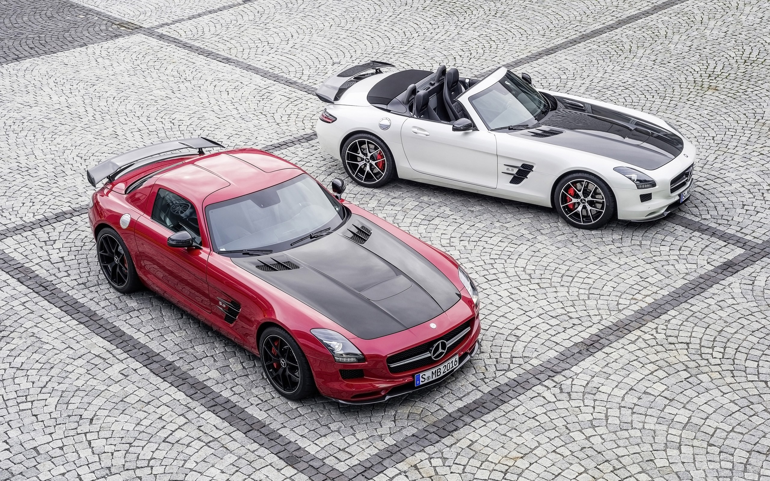 Two Mercedes-Benz SLS AMG sports cars on cobblestone HD Wallpaper
