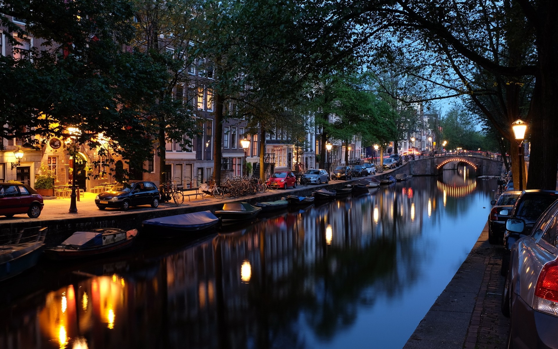 Amsterdam canal at night with illuminated bridge and buildings HD Wallpaper