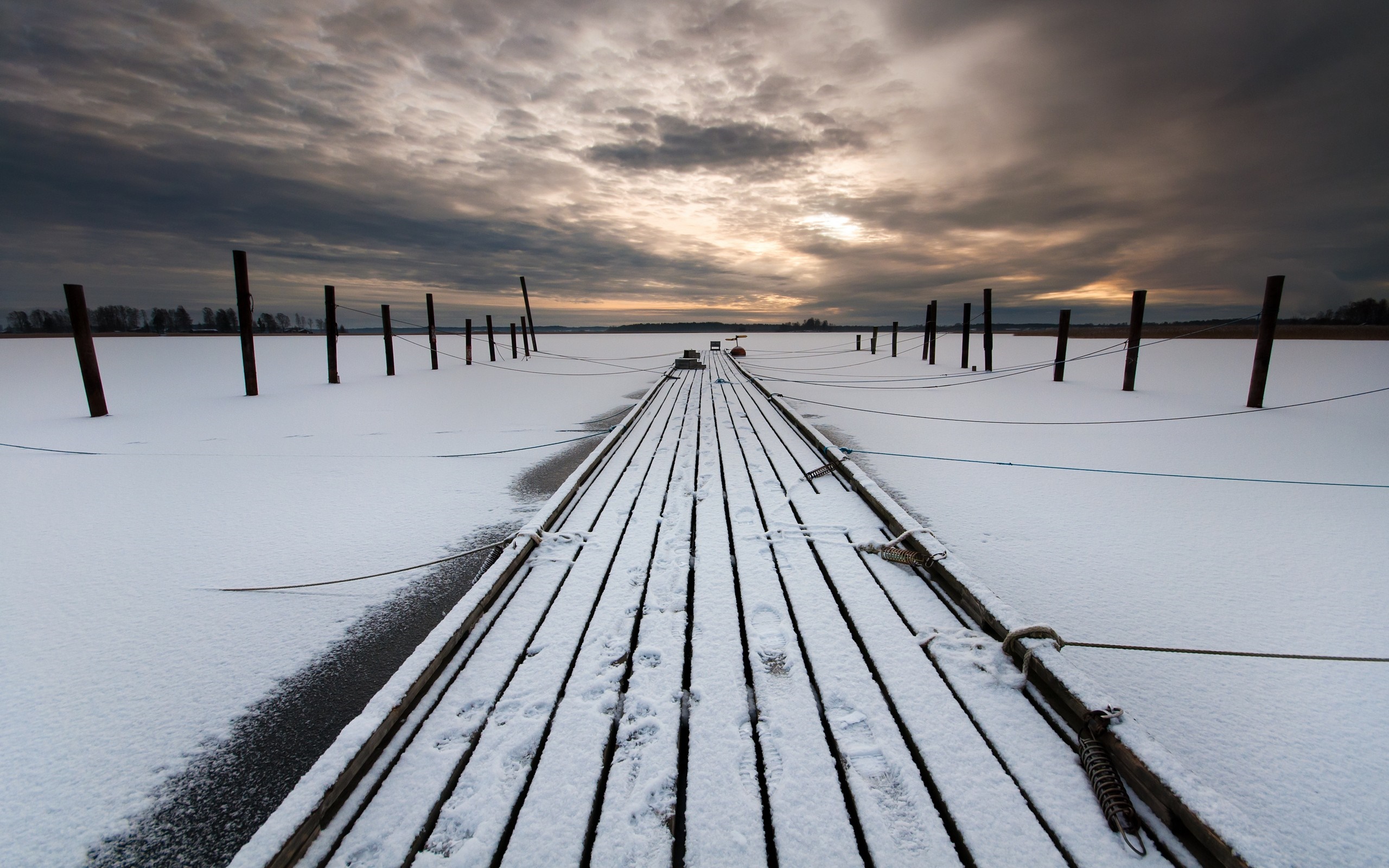 Wooden pier covered in snow on a frozen lake at sunset HD Wallpaper