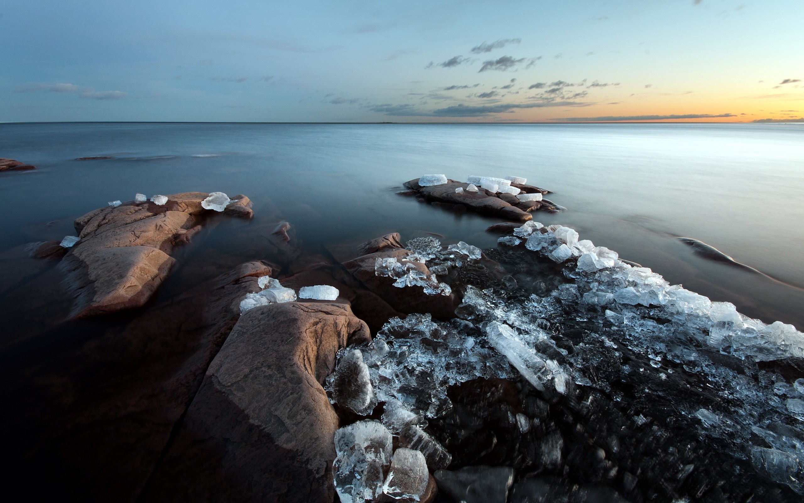 Ice and rocks on the shore of a calm body of water at dusk HD Wallpaper