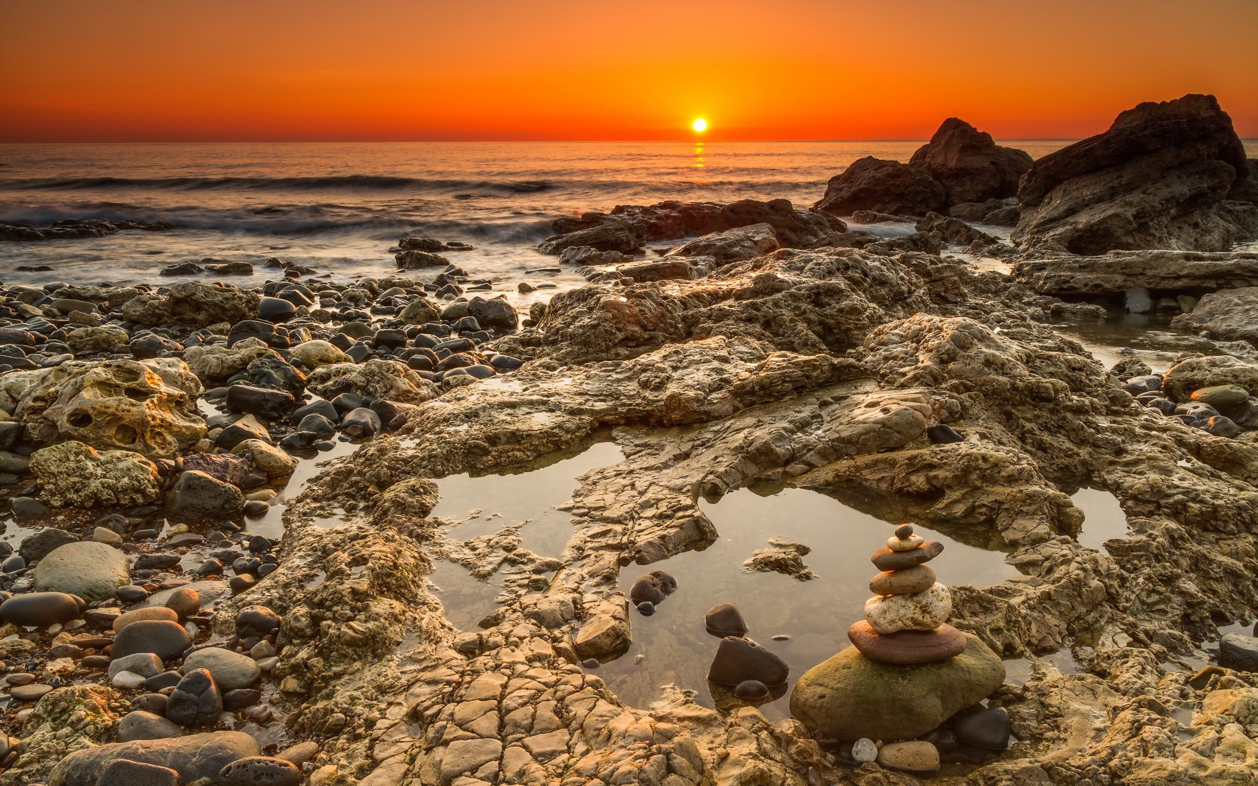 Sunset over rocky shore with stacked stones HD Wallpaper