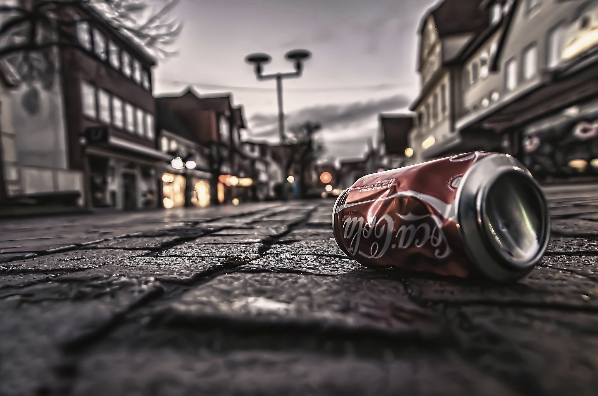 Crushed Coca-Cola can on cobblestone street HD Wallpaper