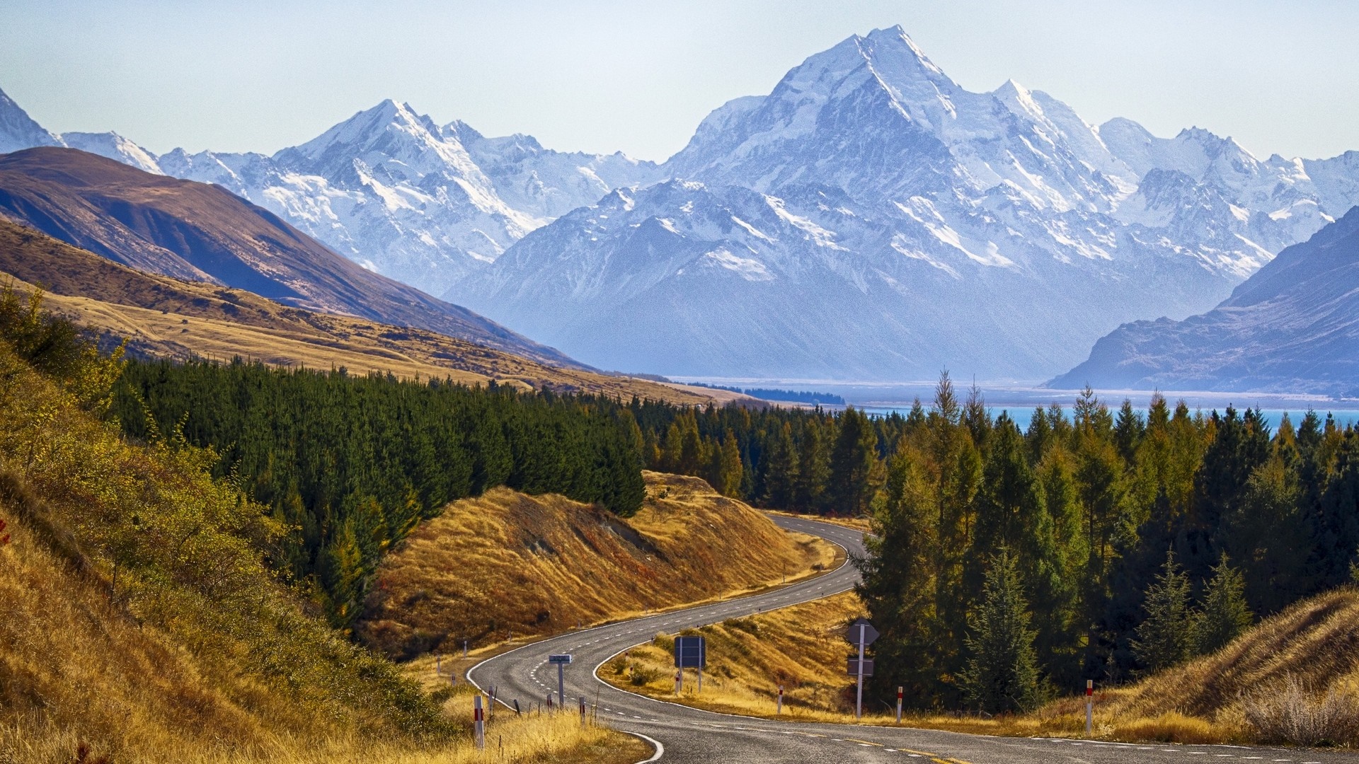 Winding road through autumn landscape towards snow-capped mountains HD Wallpaper