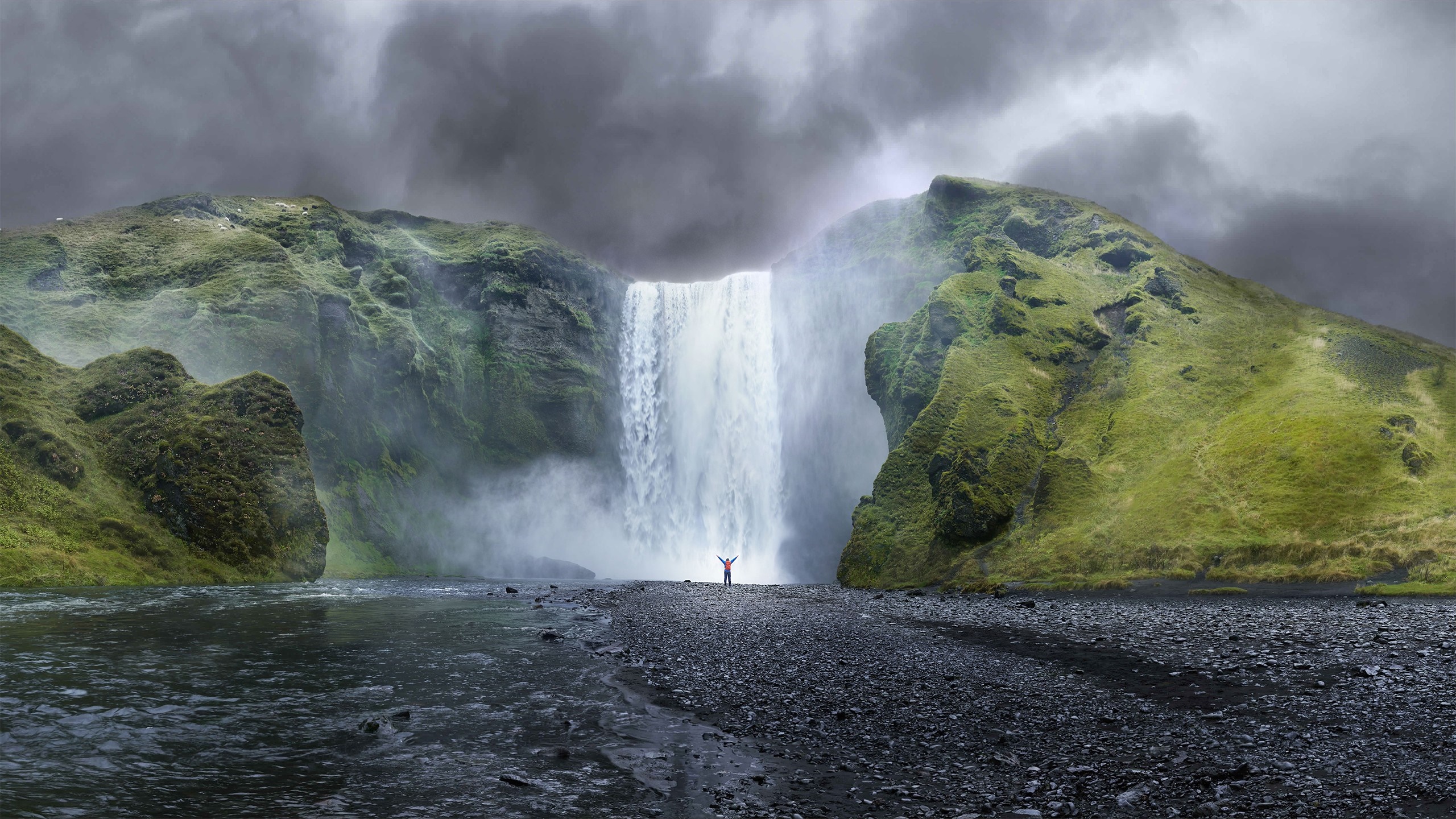 Person standing in front of a large waterfall in Iceland HD Wallpaper