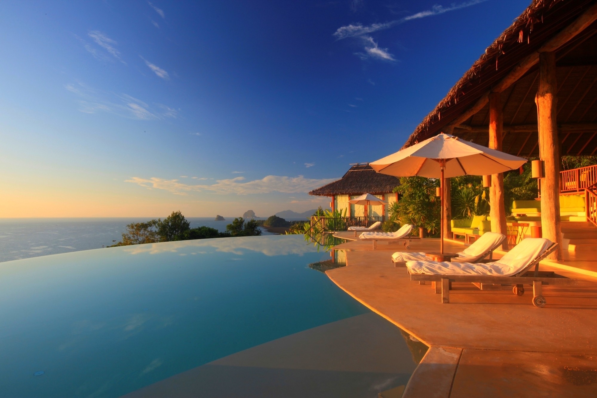 Infinity pool overlooking the ocean at sunset with lounge chairs HD Wallpaper
