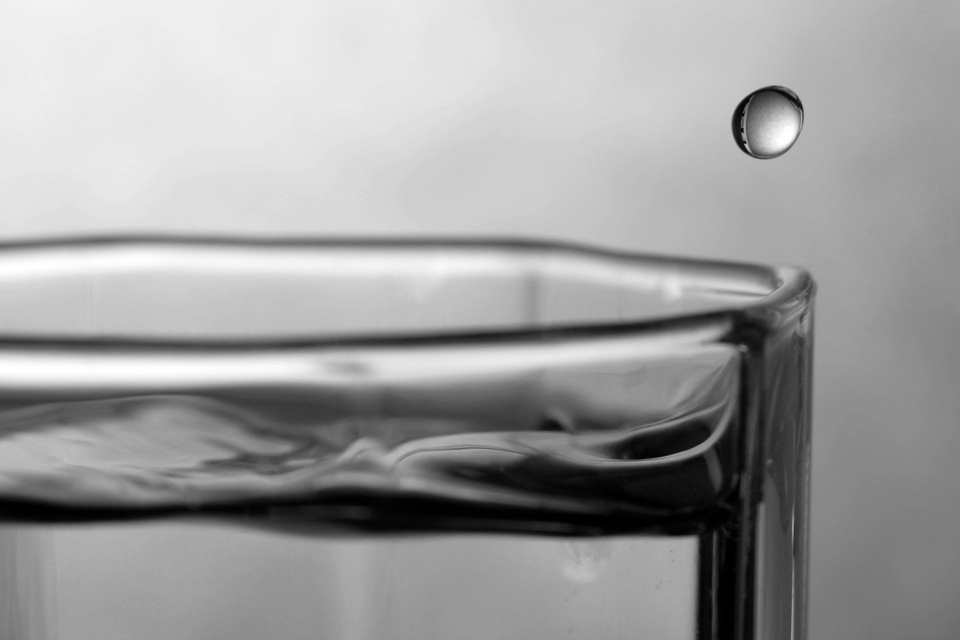 Monochrome photography of a water drop above a glass HD Wallpaper