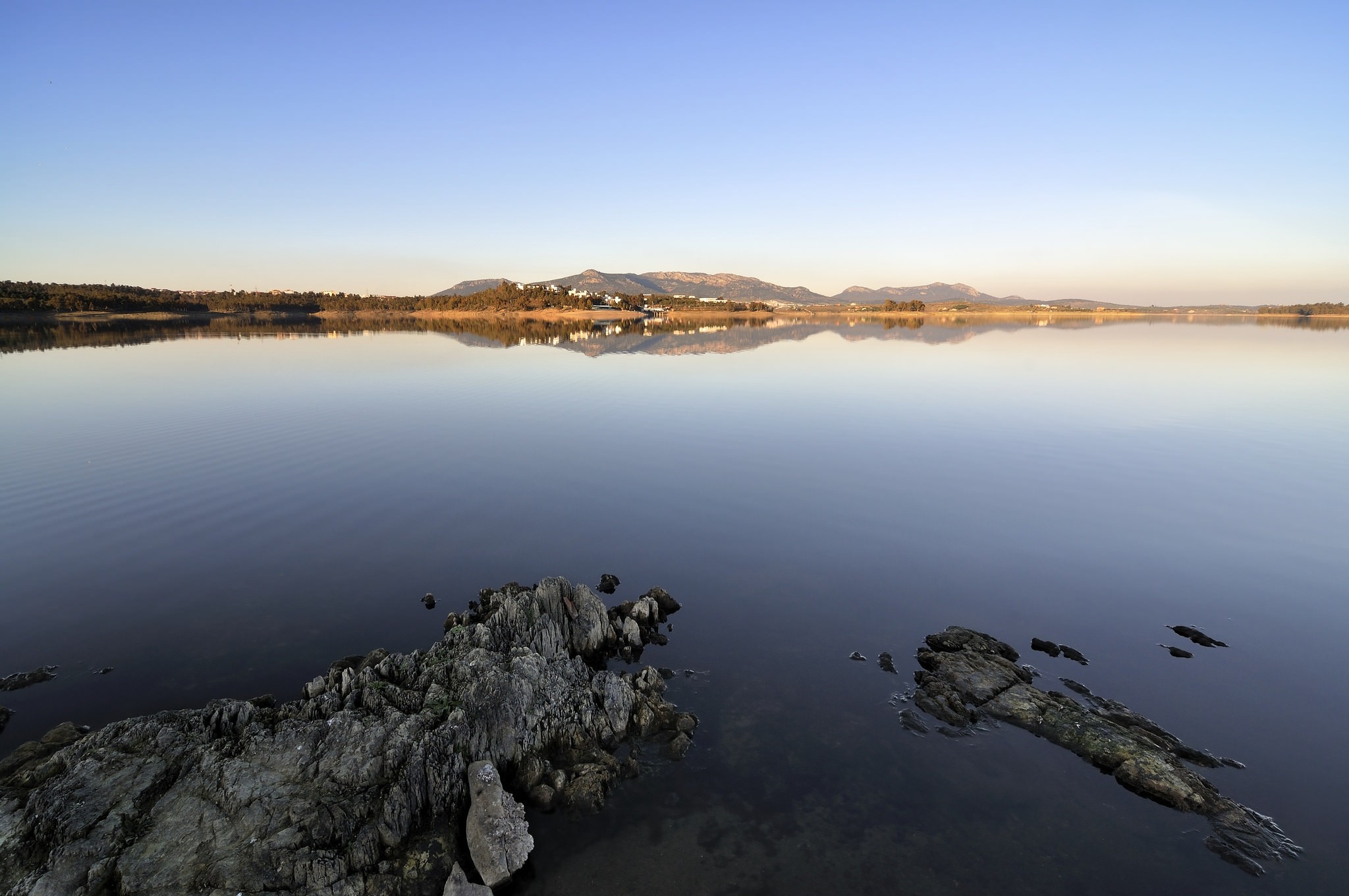 Calm lake with distant mountains and rocky shore HD Wallpaper