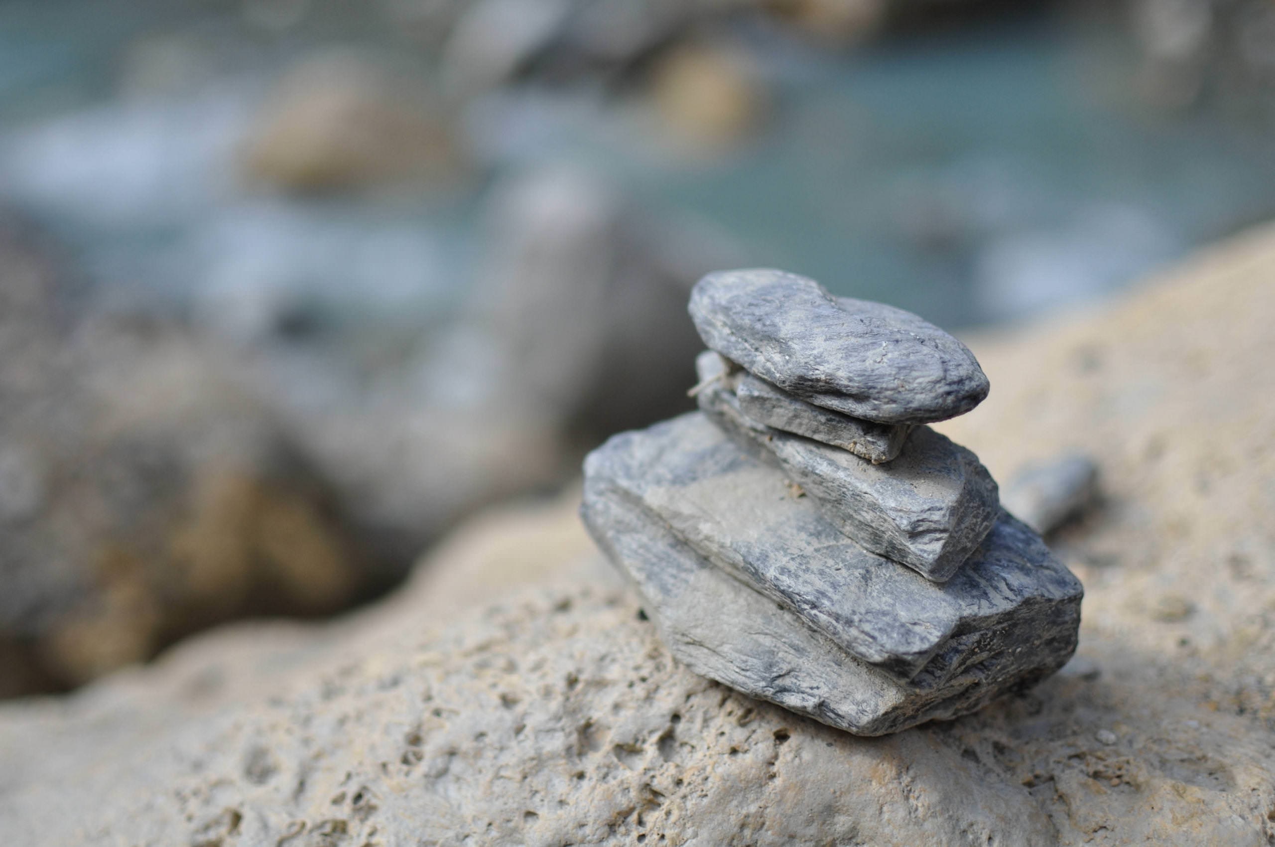 Stack of stones on a rocky shore with blurred water background HD Wallpaper
