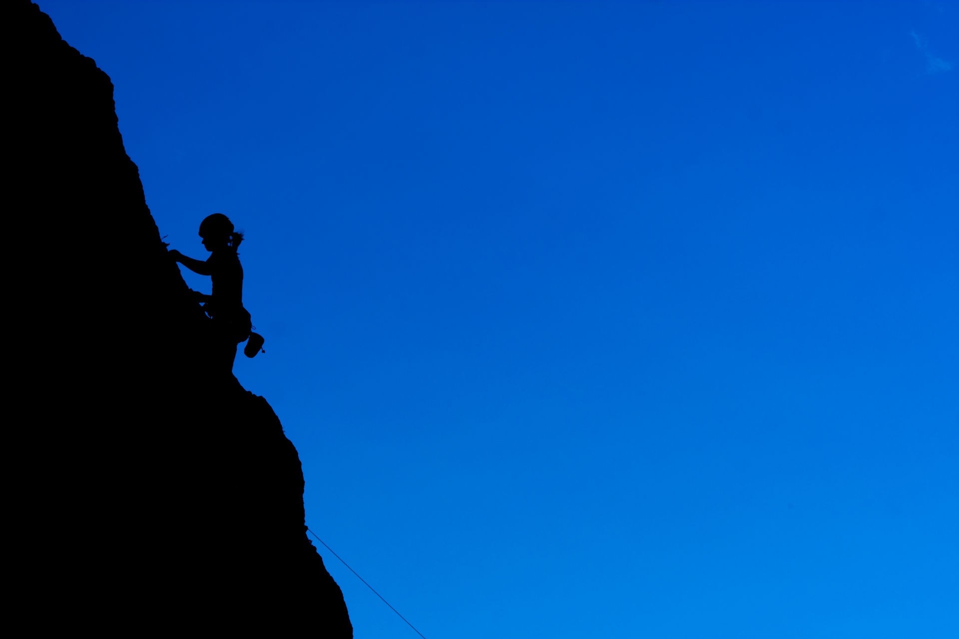 Silhouette of a person rock climbing against a blue sky HD Wallpaper