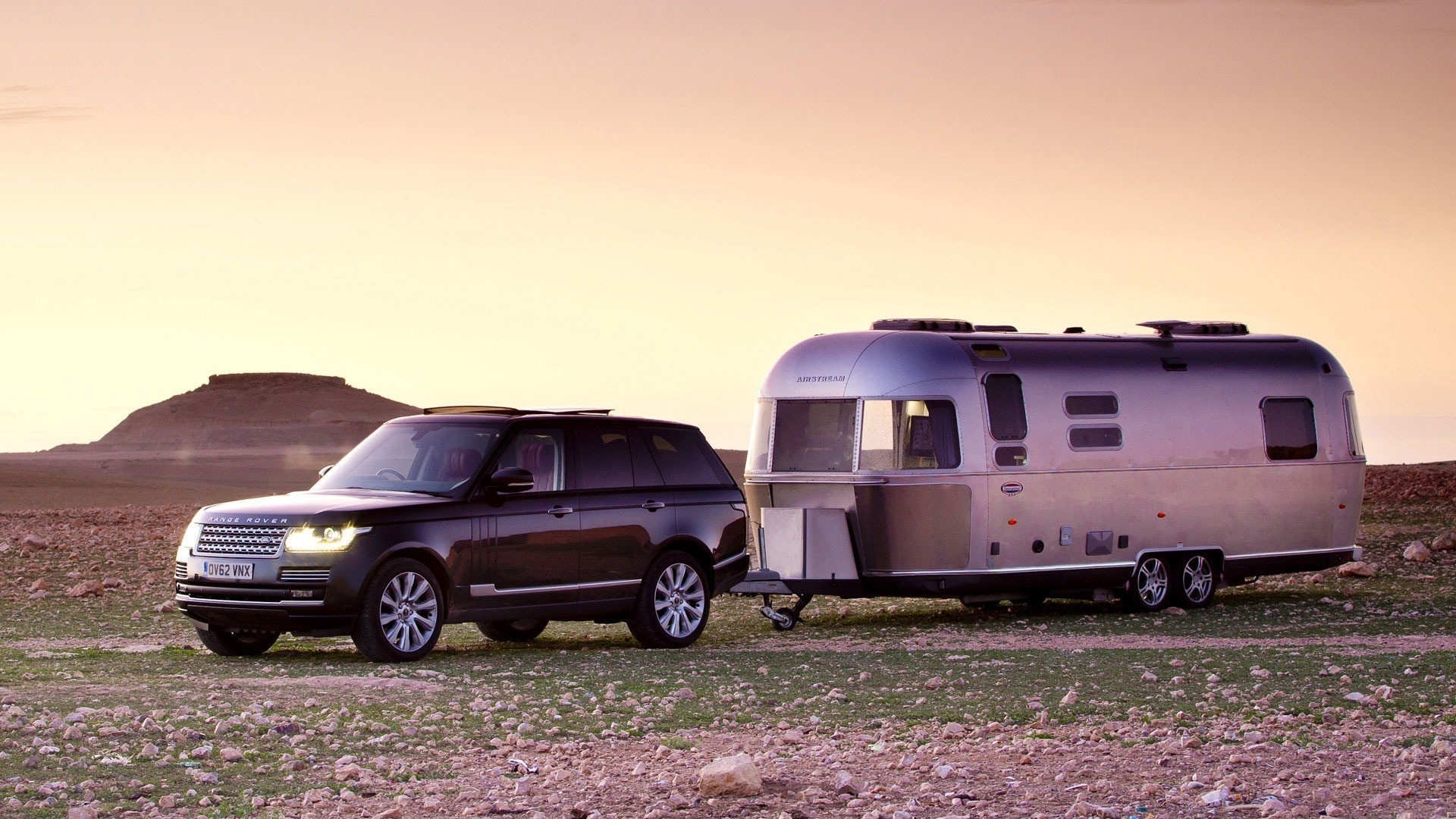 Range Rover towing an Airstream trailer in a desert landscape HD Wallpaper