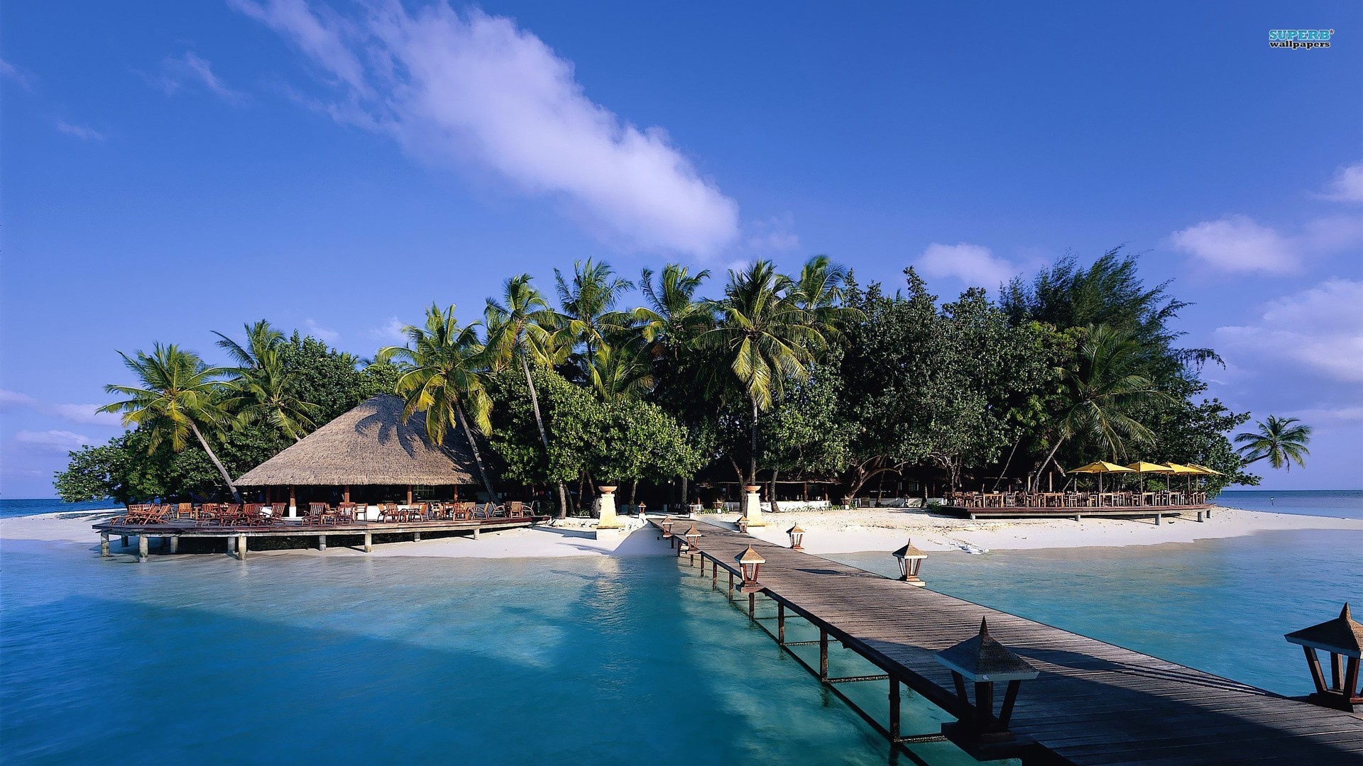 Tropical island resort with thatched-roof building and pier HD Wallpaper