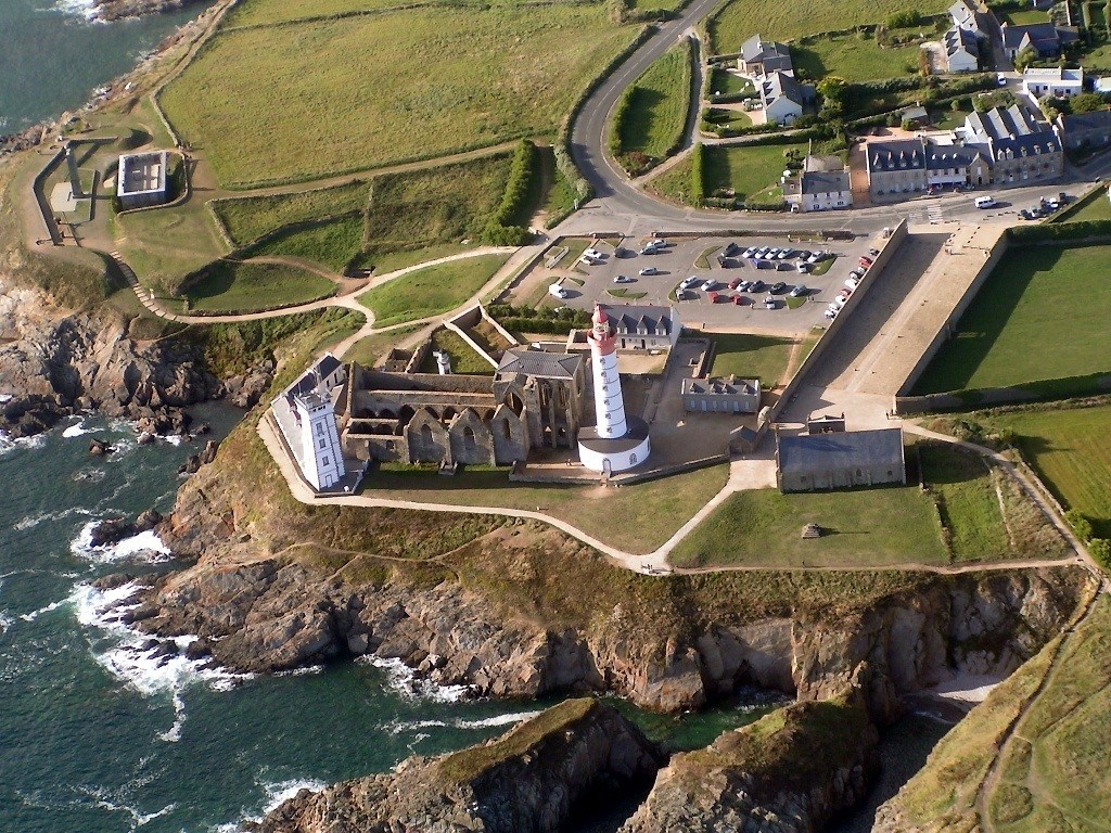 Aerial view of a lighthouse and ruins on a rocky coast HD Wallpaper