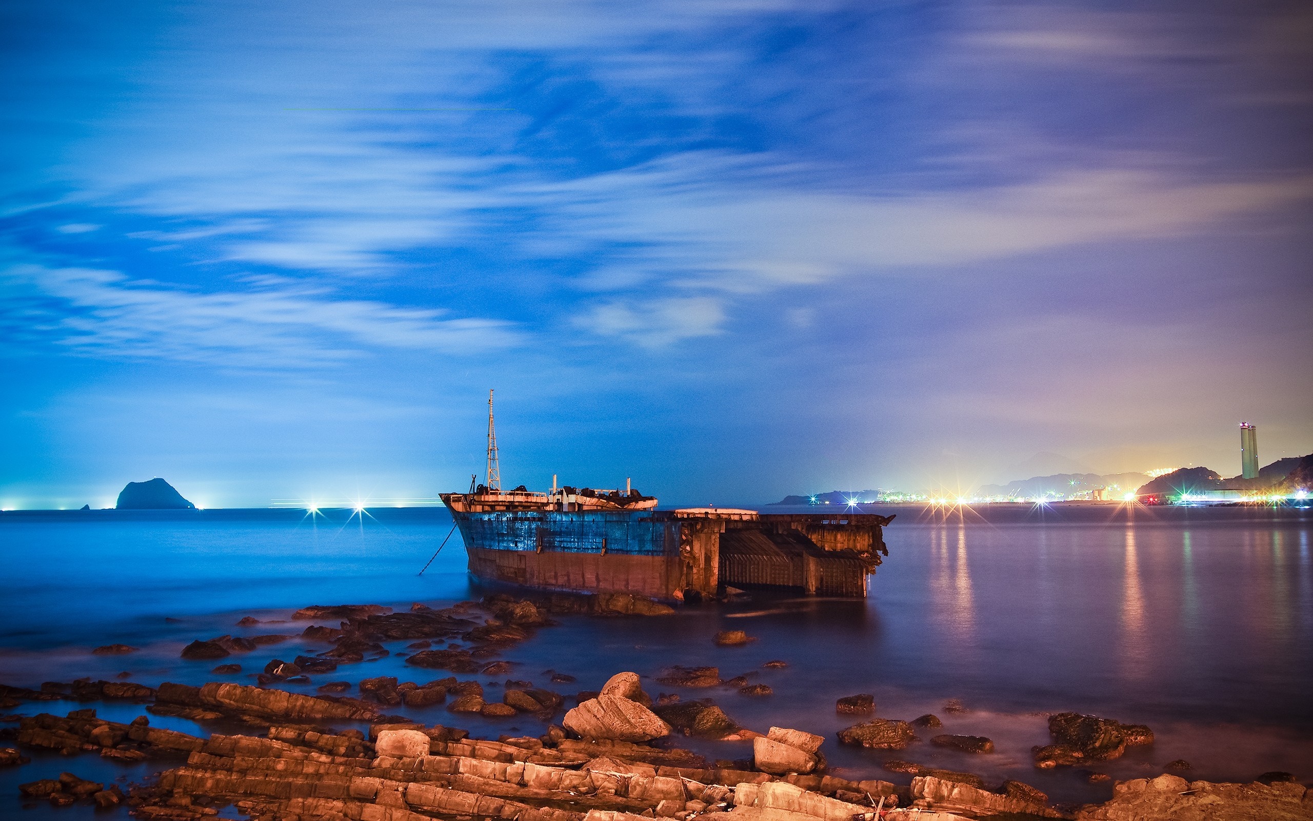 Shipwreck at night with distant cityscape and island HD Wallpaper