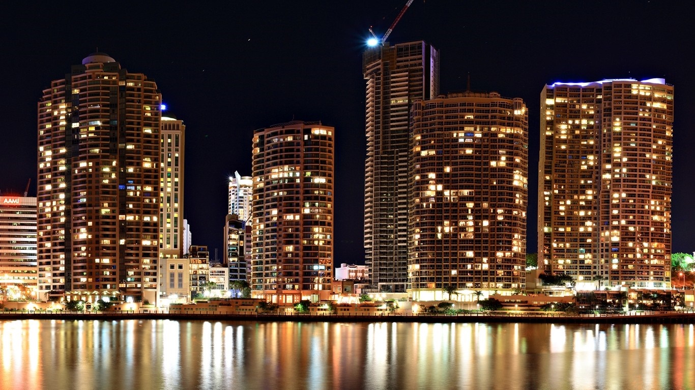 Cityscape at night with illuminated skyscrapers and water reflections HD Wallpaper