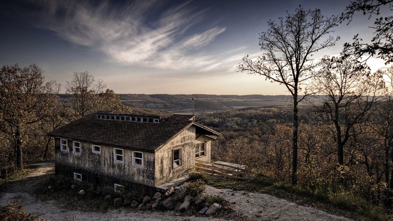 Rustic cabin on a hill overlooking a forest landscape at sunset HD Wallpaper