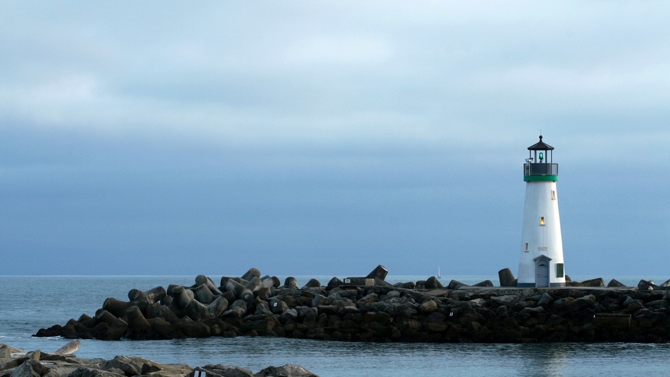 White lighthouse on a breakwater with ocean and cloudy sky HD Wallpaper