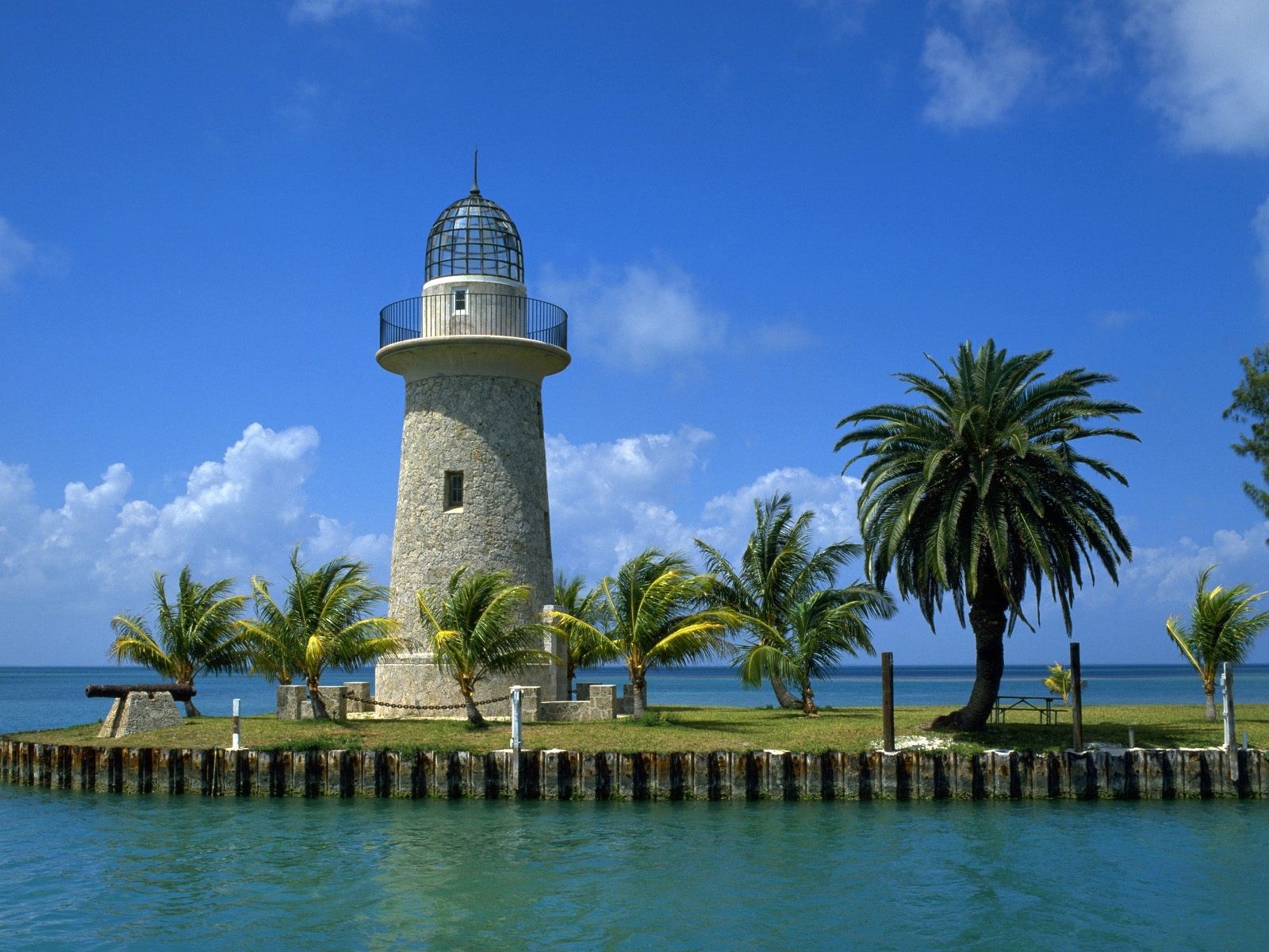 Stone lighthouse on an island with palm trees and the sea HD Wallpaper