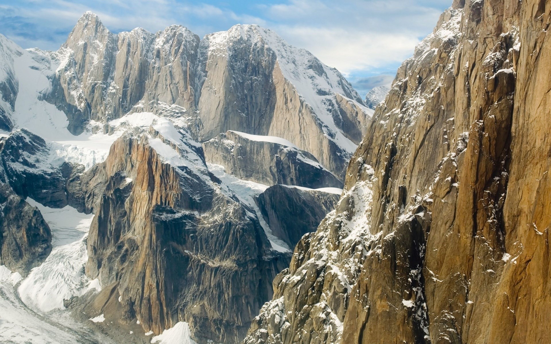 Snow-covered rocky mountains under a cloudy sky HD Wallpaper
