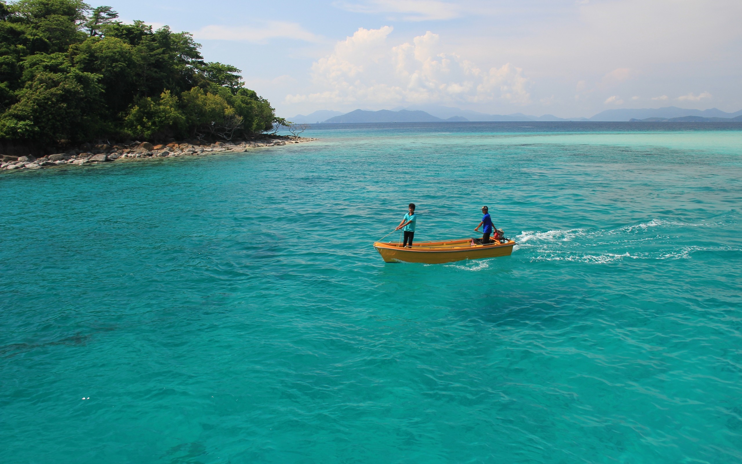 Two people in a yellow boat on turquoise water near an island HD Wallpaper