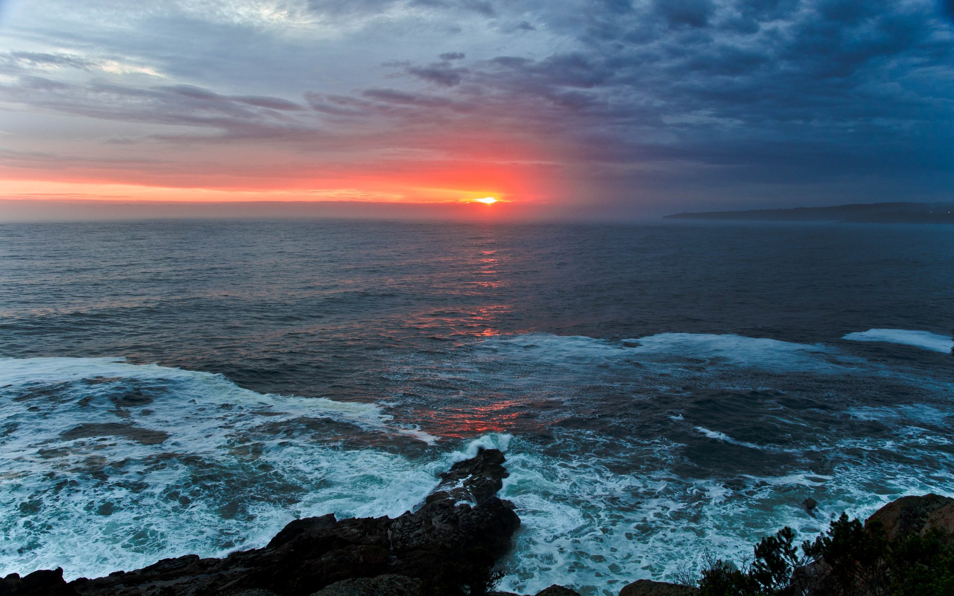 Sunset over the ocean with waves crashing on rocks HD Wallpaper