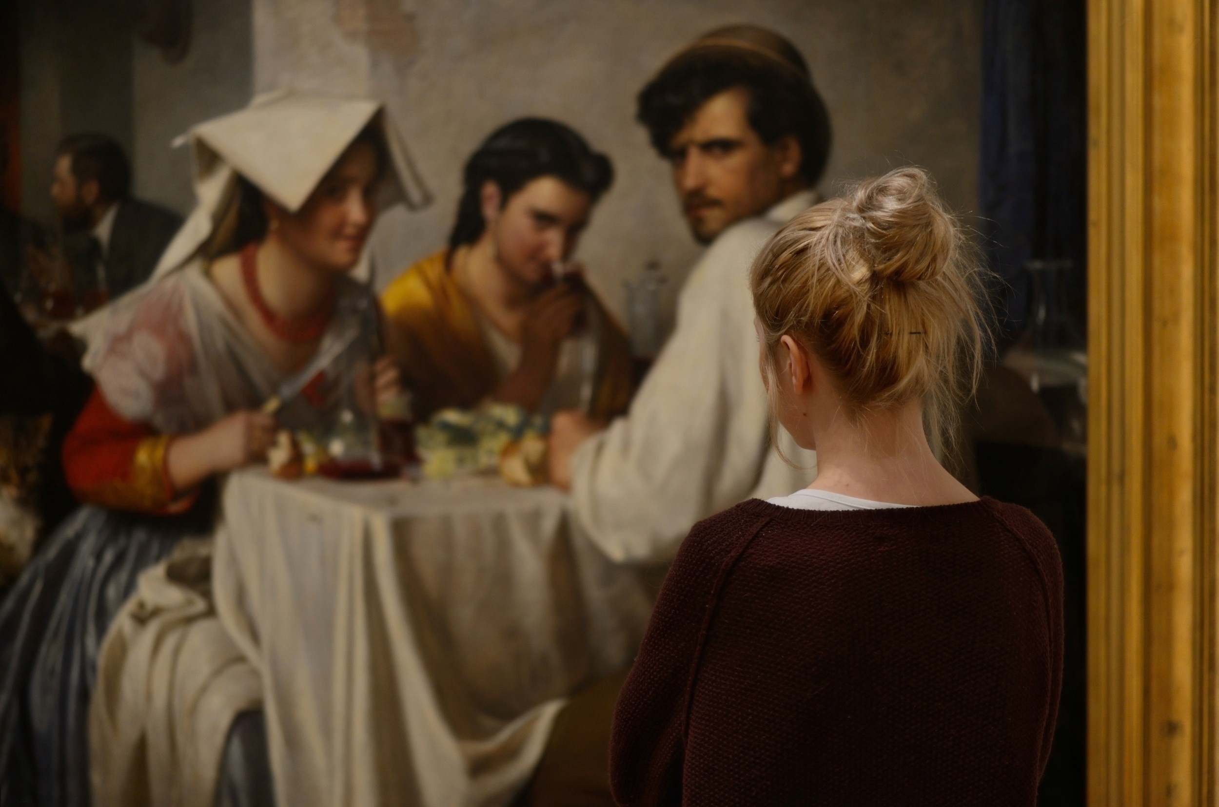Woman looking at a painting of people at a table HD Wallpaper