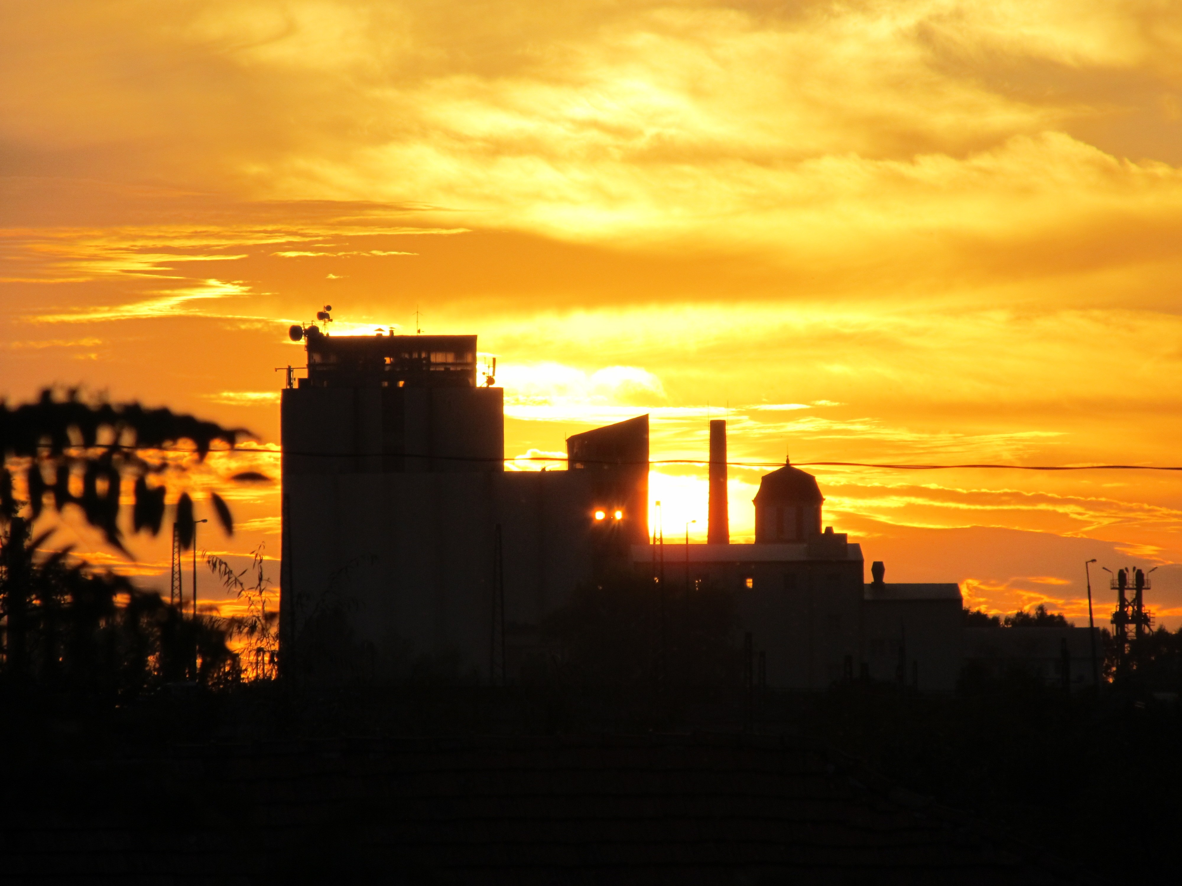 Industrial buildings silhouetted against a vibrant sunset sky HD Wallpaper