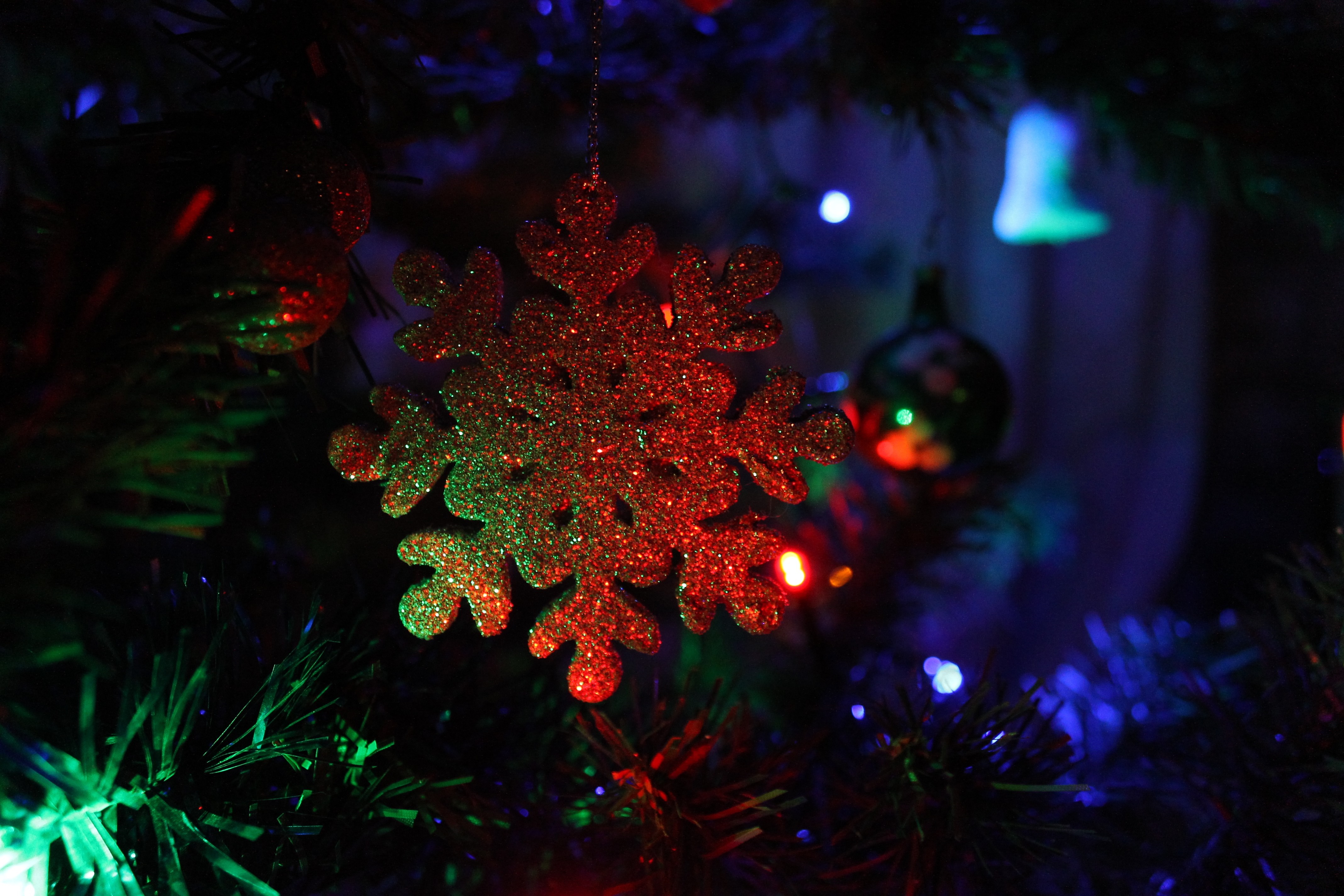 Glittering snowflake ornament on a Christmas tree with lights HD Wallpaper