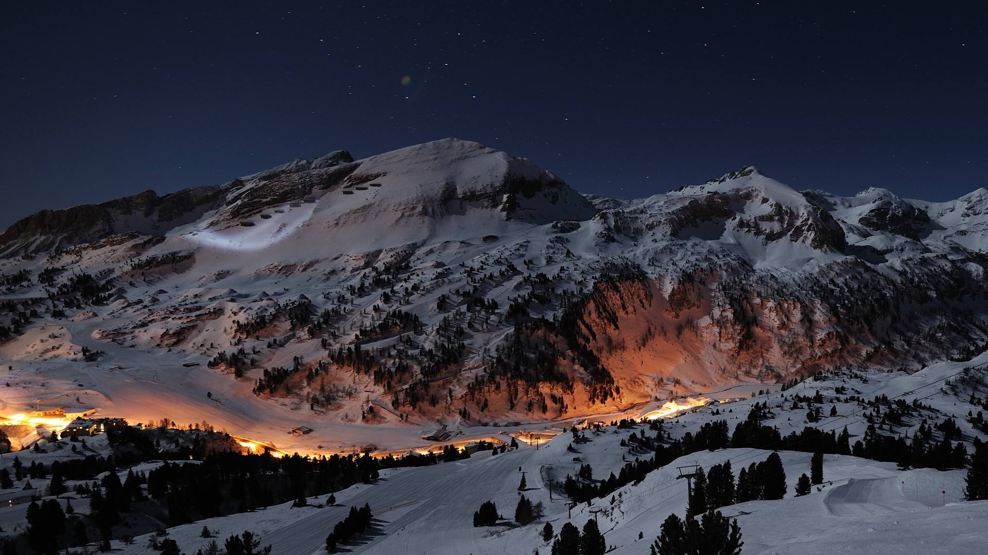 Snowy mountains at night with village lights HD Wallpaper