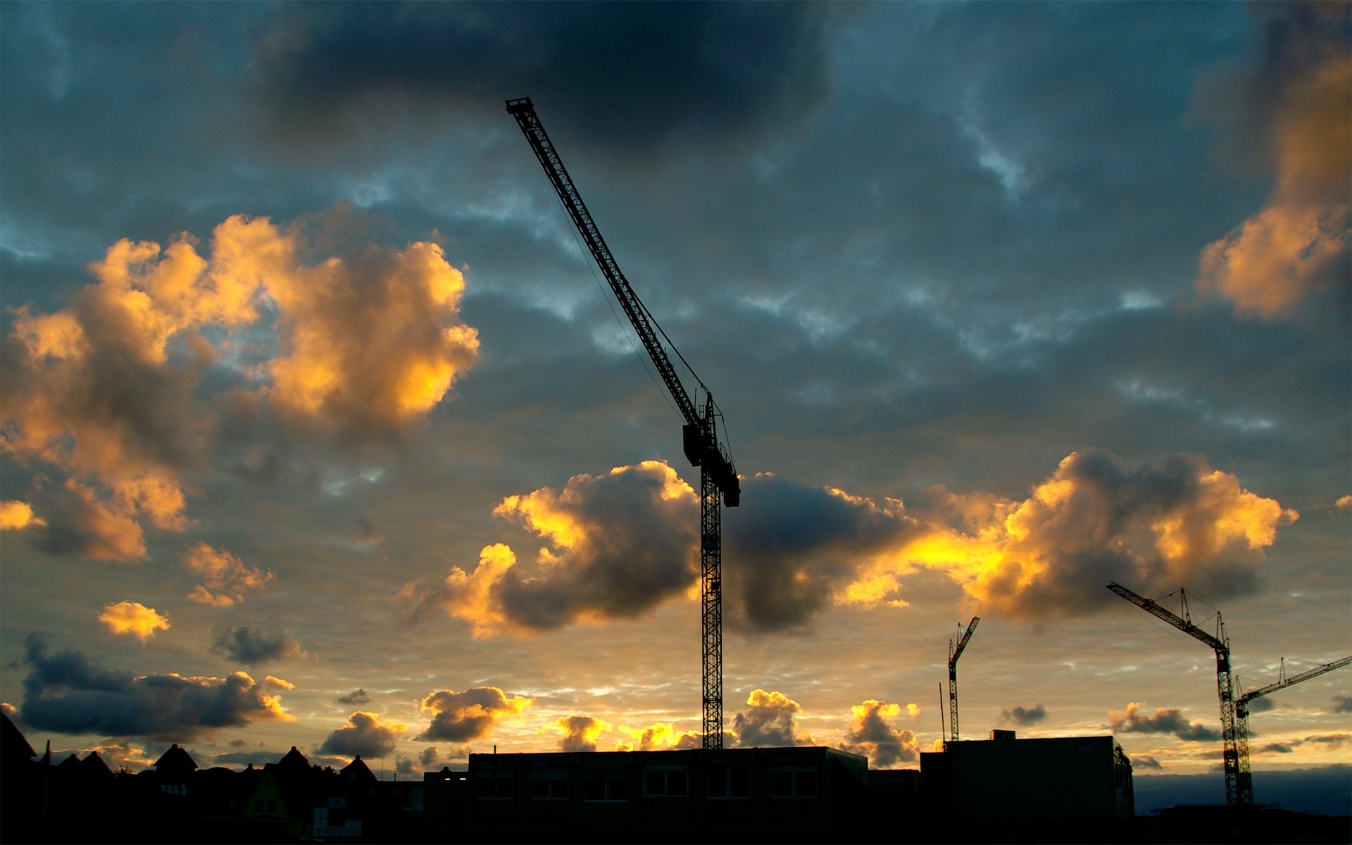 Silhouette of construction cranes against a dramatic sunset sky HD Wallpaper