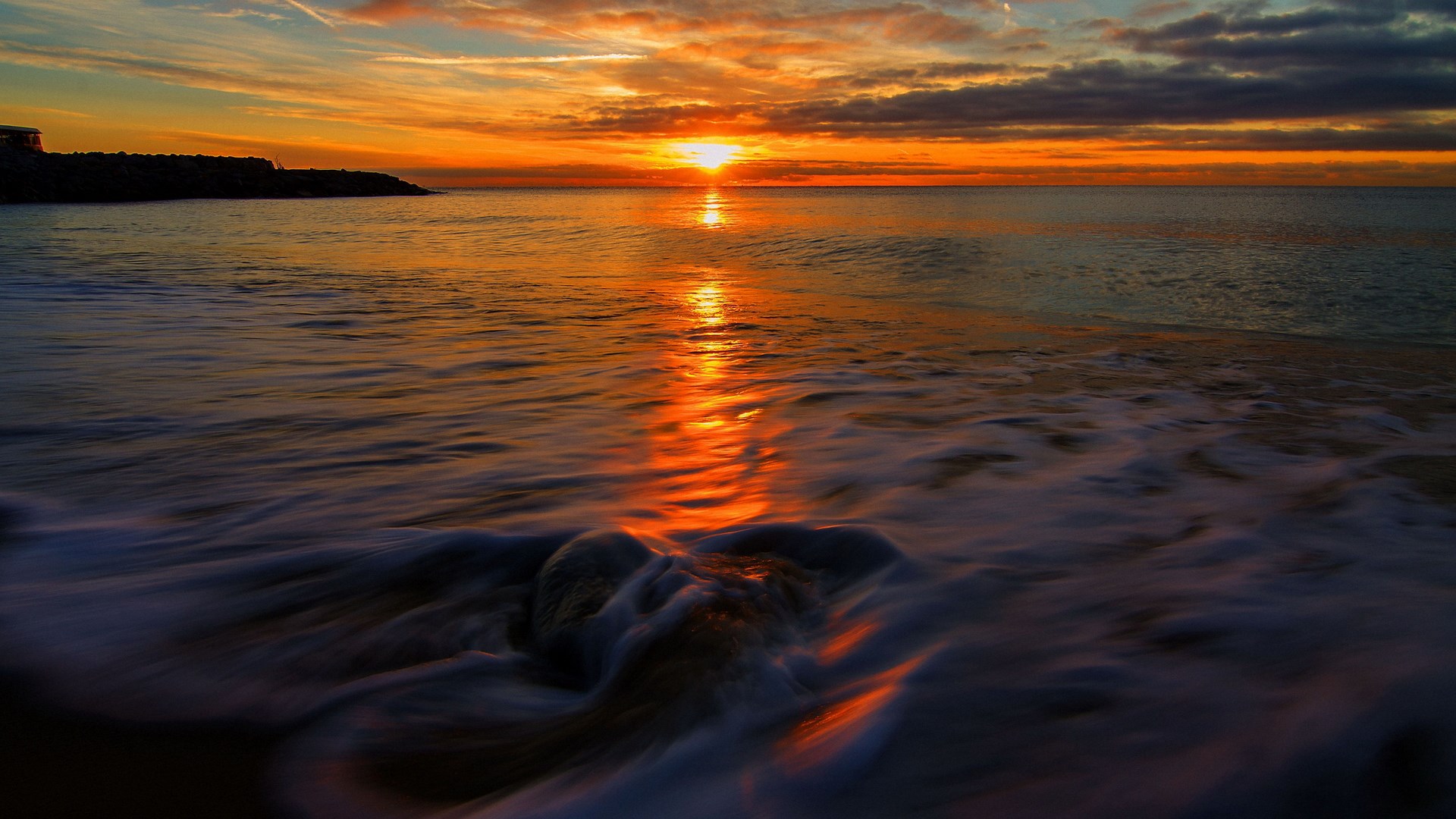 Sunset over the ocean with waves crashing on rocks HD Wallpaper