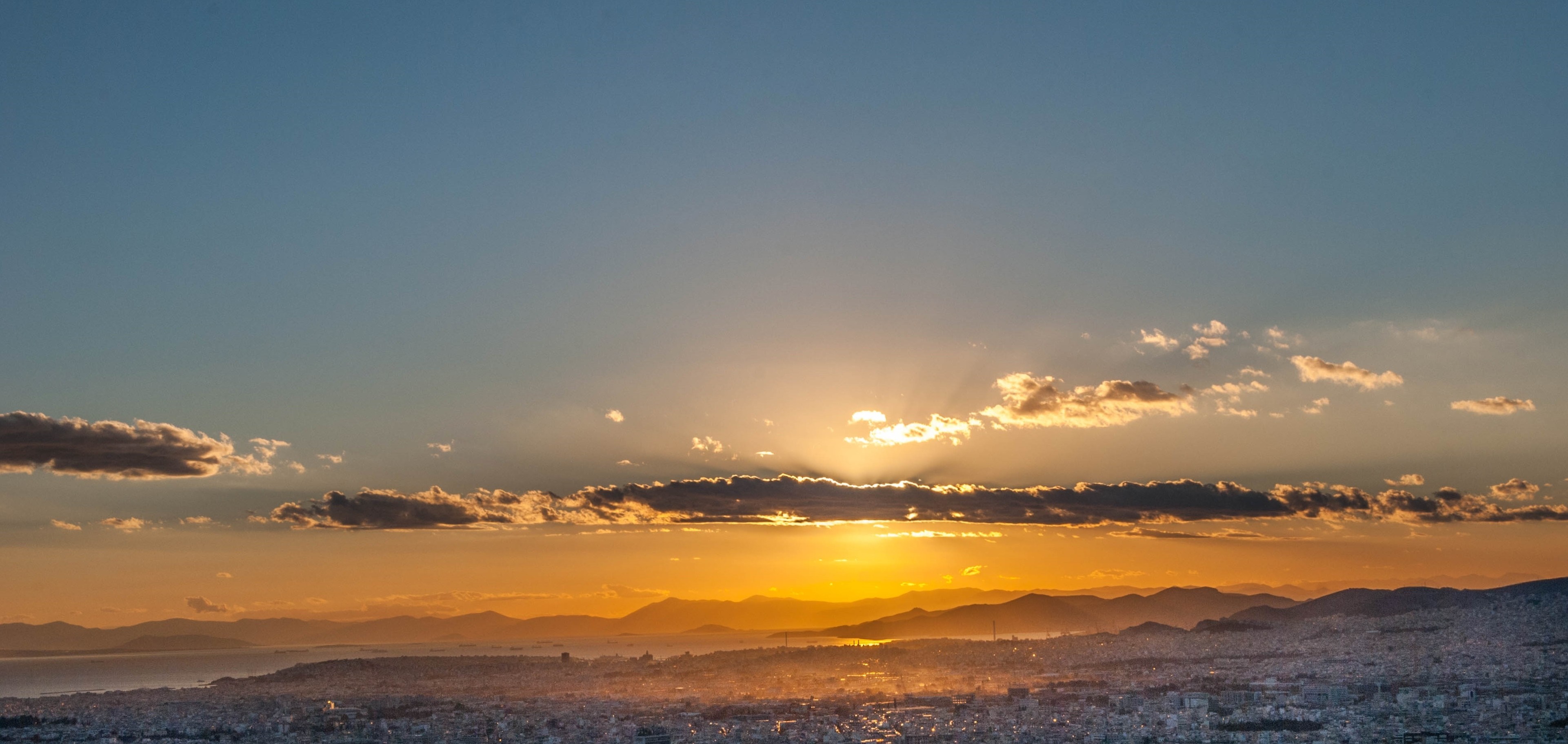 Sunset over a coastal cityscape with mountains on the horizon HD Wallpaper