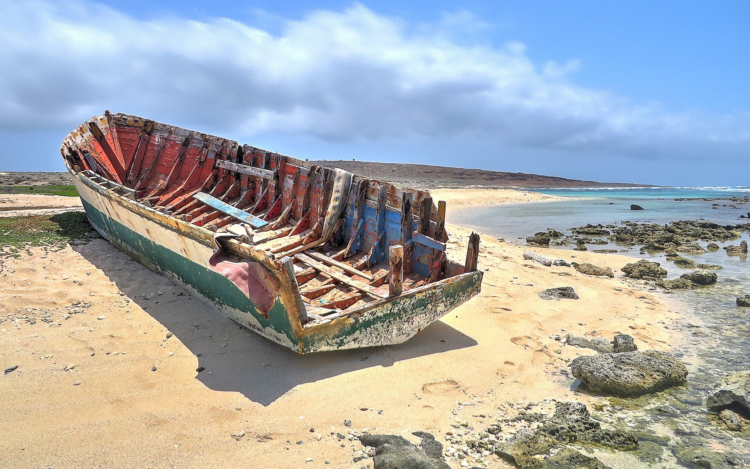 Wrecked wooden boat on a sandy beach with ocean in background HD Wallpaper